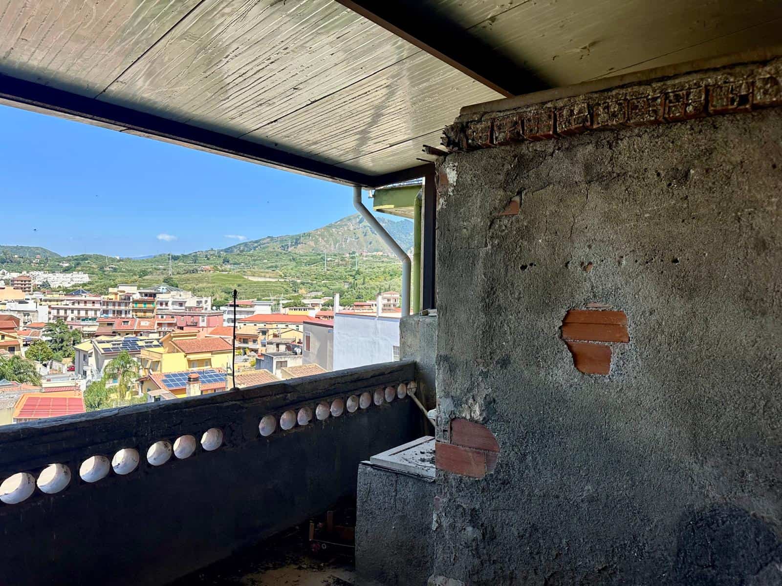 Balcone di un edificio in costruzione con vista sulle case e sulla natura circostante, muratura grezza e parti in fase di ristrutturazione.