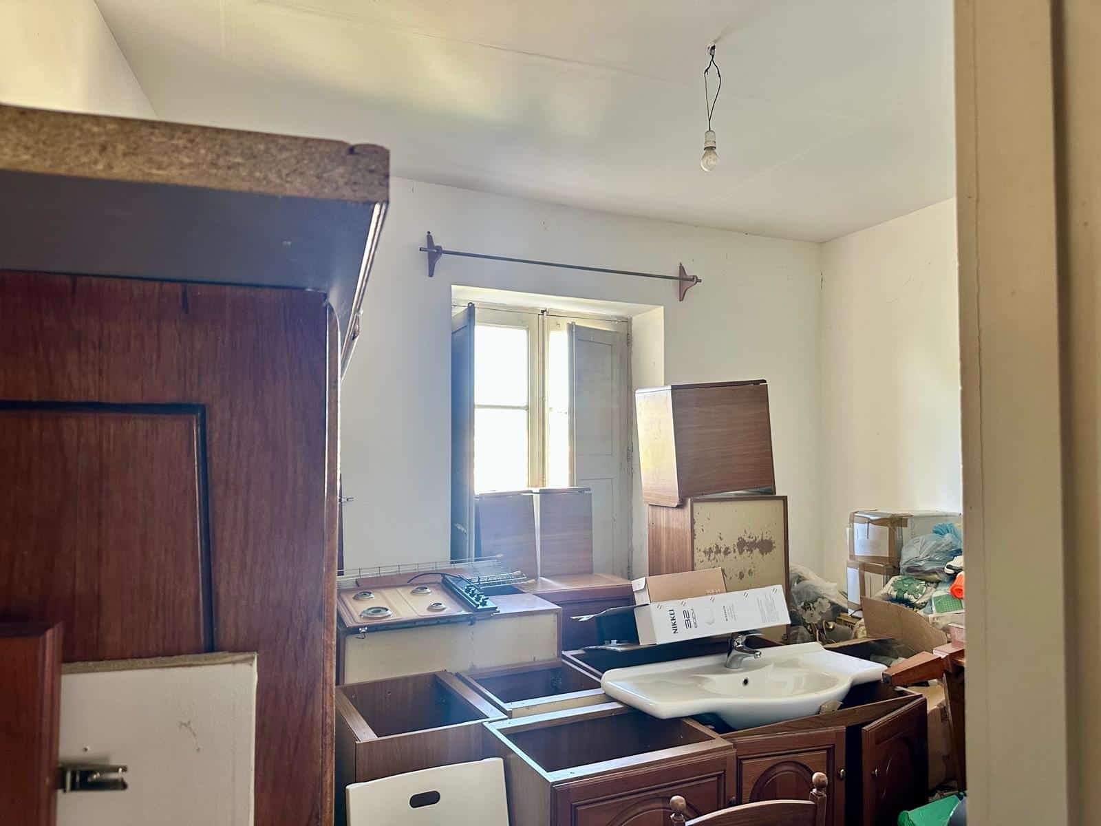 Vecchia cucina con mobili in legno, lavandino e scatole di stoccaggio, ambiente in attesa di ristrutturazione in una casa storica.