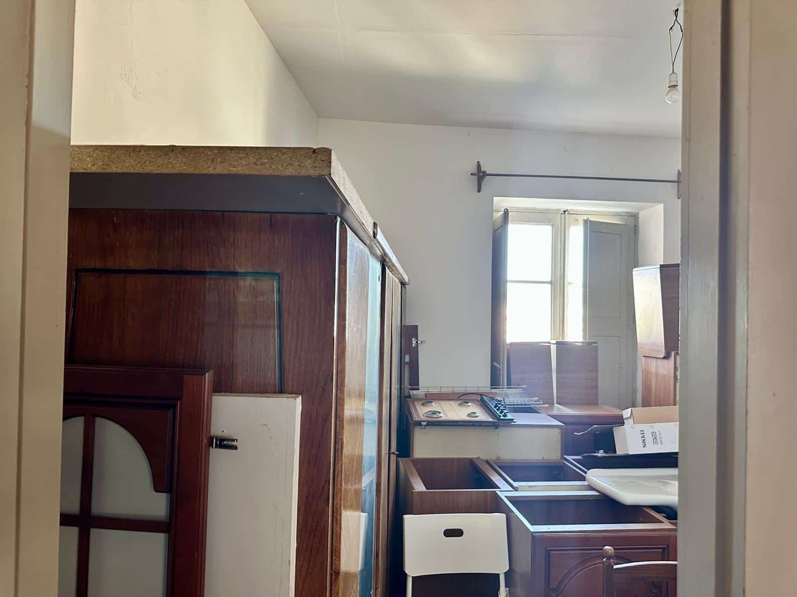 Vecchio mobili da cucina in legno con piano in cemento, finestra con persiana, ambiente abitativo da ristrutturare, immagine di interni casa privata.