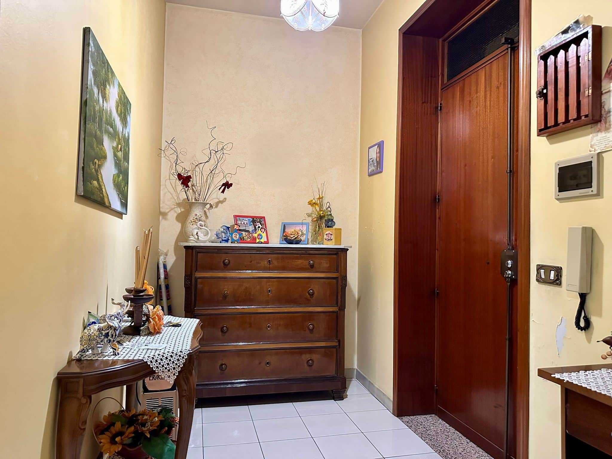 Ripostiglio o ingresso con mobile in legno, decorazioni floreali e quadri, ambiente accogliente e funzionale, perfetto come zona di passaggio o deposito.