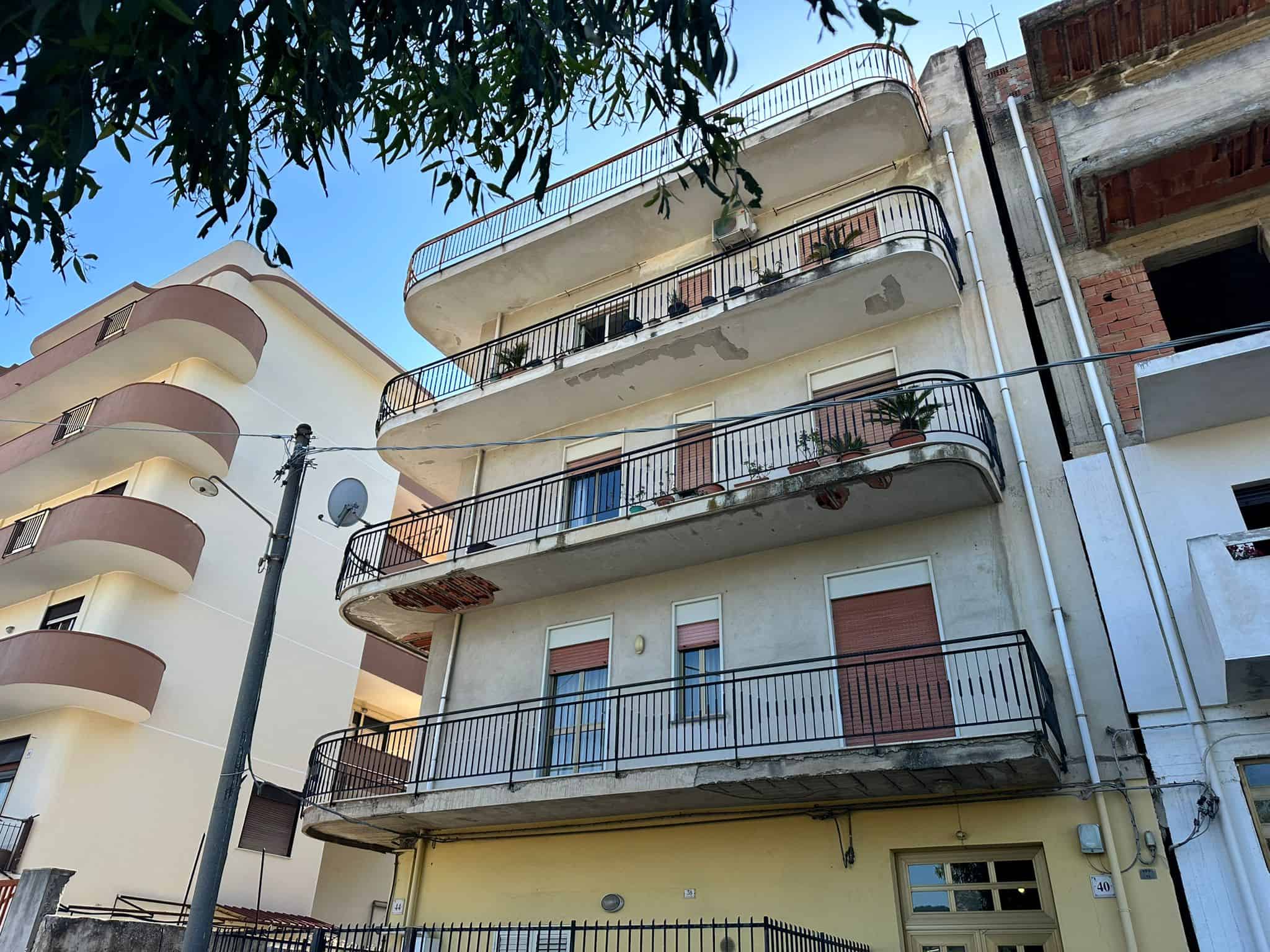 Villetta residenziale con balconi e piante in vaso, edificio multifamiliare in fase di ristrutturazione o manutenzione, architettura urbana contemporanea, immobile in quartiere residenziale.