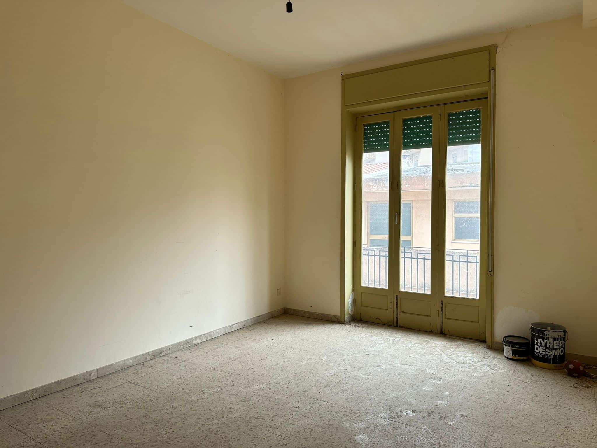 Ampio soggiorno con porta finestra che dà su balcone, pareti beige e pavimento in gres, ambiente luminoso e da personalizzare, ideale per abitazione o investimento immobiliare.