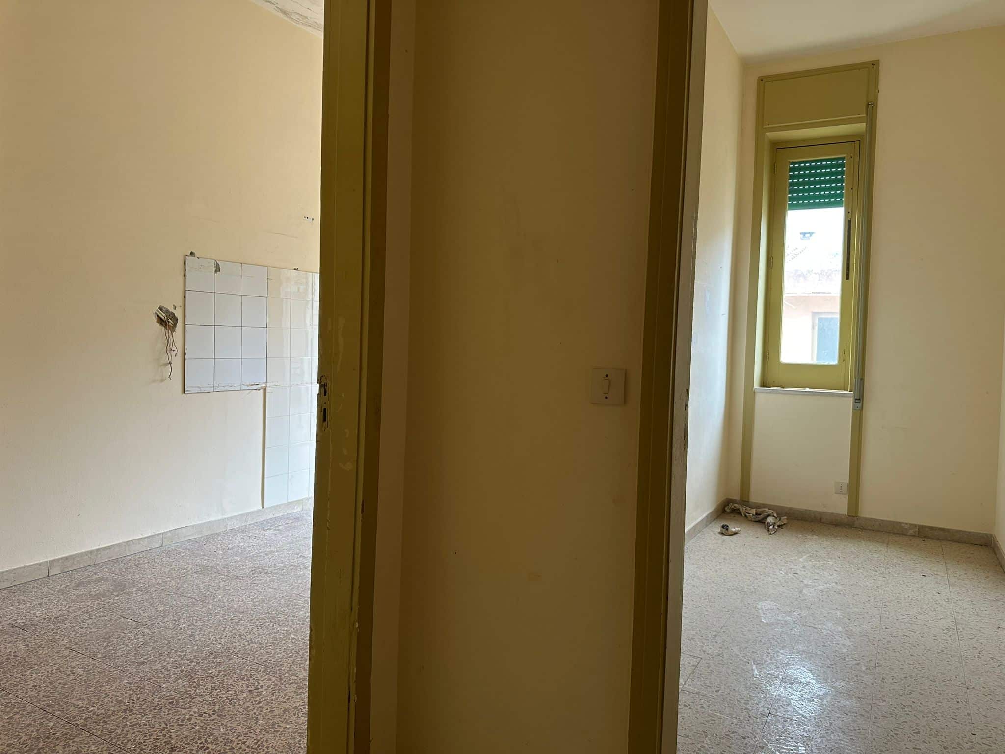 Interno di appartamento in fase di ristrutturazione, pareti beige e finestre con cornici gialle, pavimento in marmo, ambiente luminoso e spazioso, pronto per essere personalizzato.
