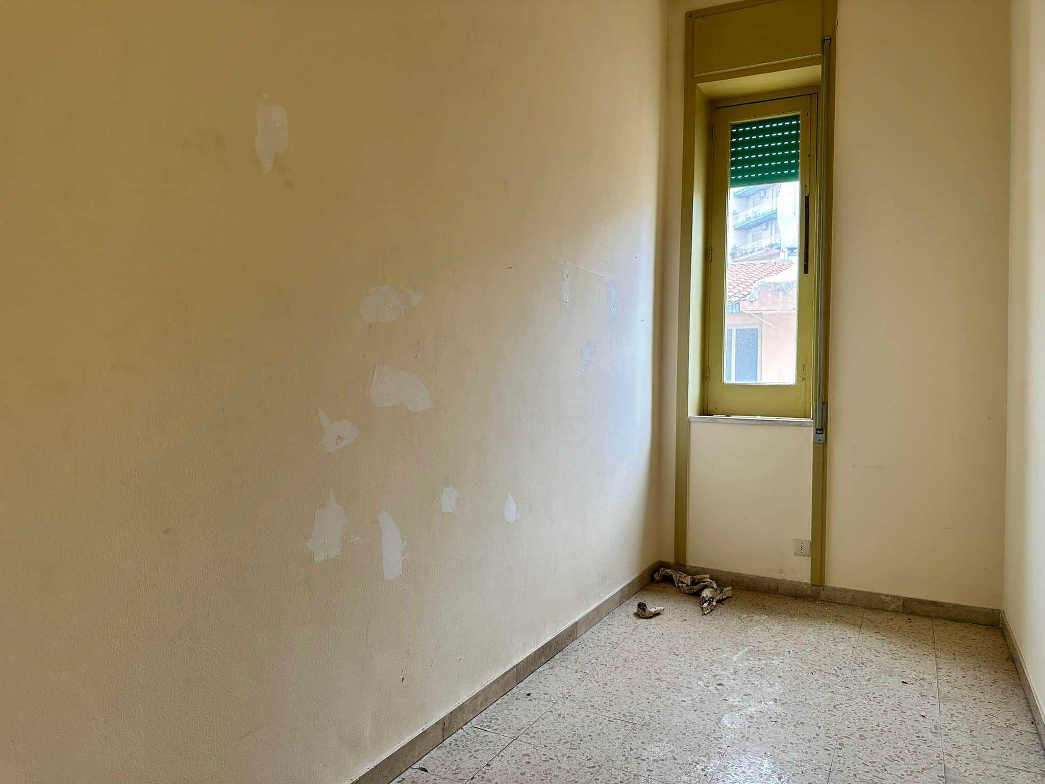 Finestra in una stanza vuota con pareti gialle e pavimento in marmo, pronta per ristrutturazione o arredamento, ideale per investimenti immobiliari e affitti.