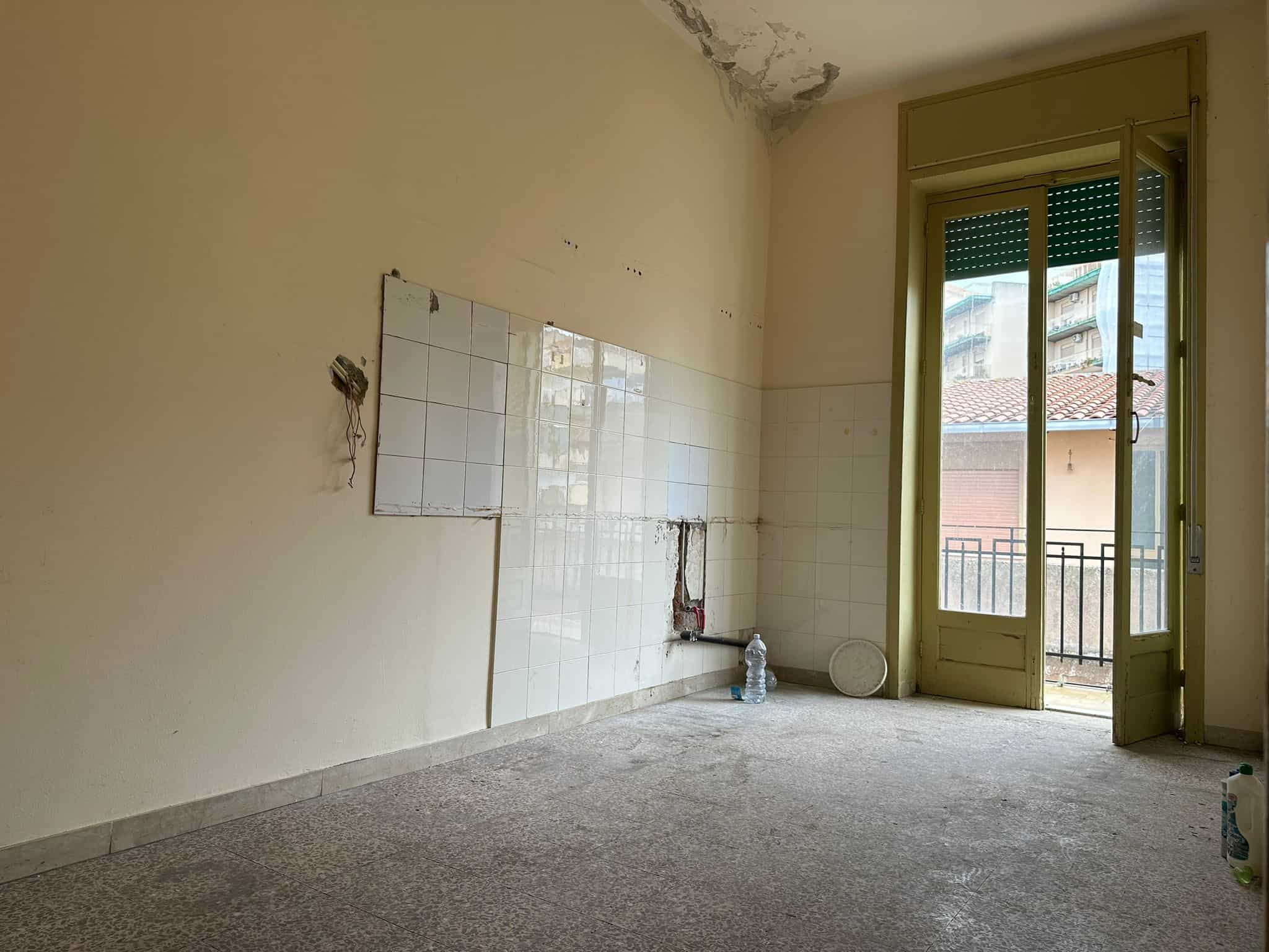 Stanza vuota in fase di ristrutturazione con pareti da riempire e finestra con balcone, pronta per essere trasformata in spaziosa cucina o soggiorno. Occasione per personalizzare gli interni di casa.