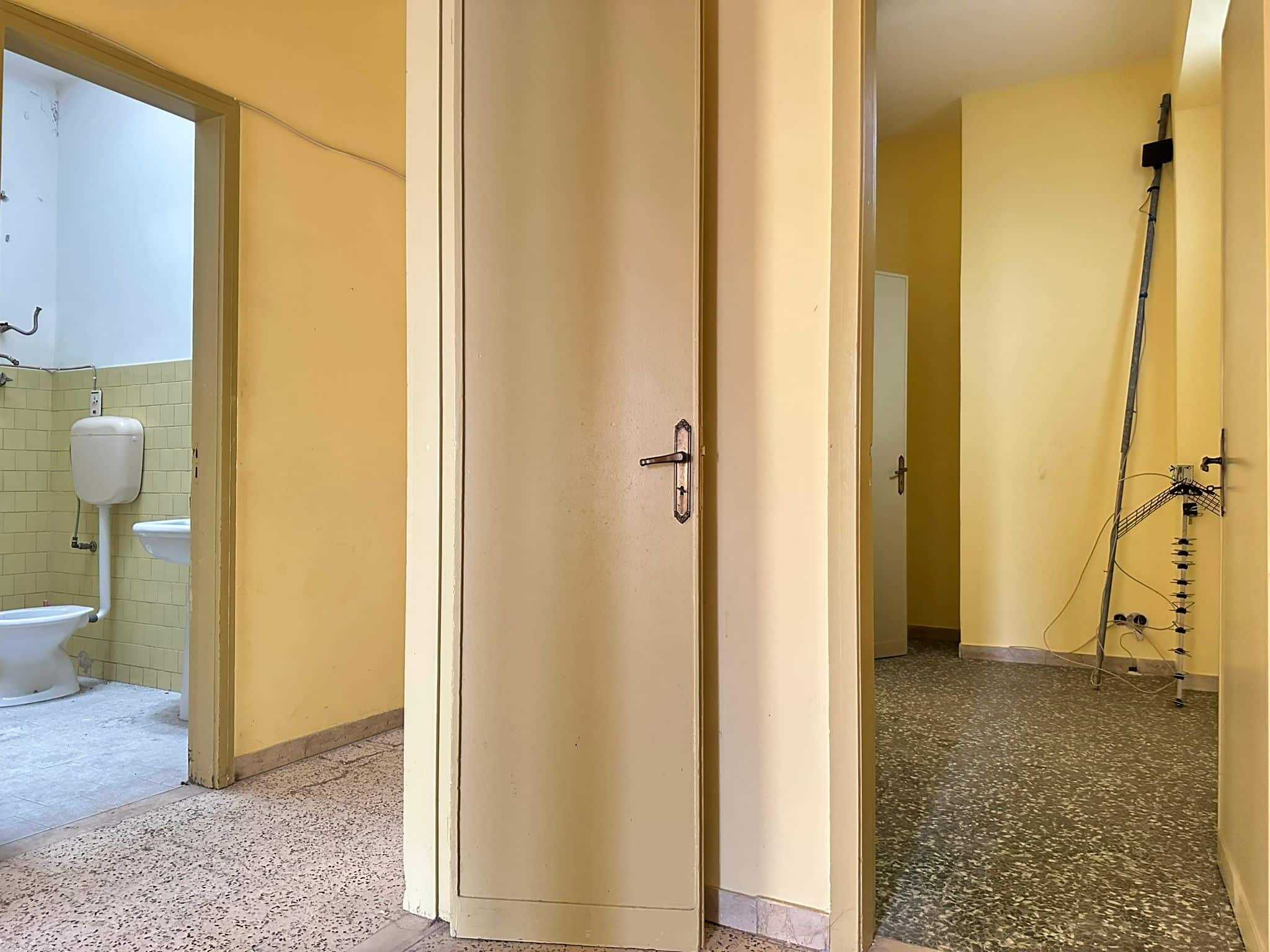 Persone che entrano in un appartamento con pareti gialle e pavimenti in gres porcellanato, mostrando le diverse stanze e un bagno con piastrelle beige chiaro.
