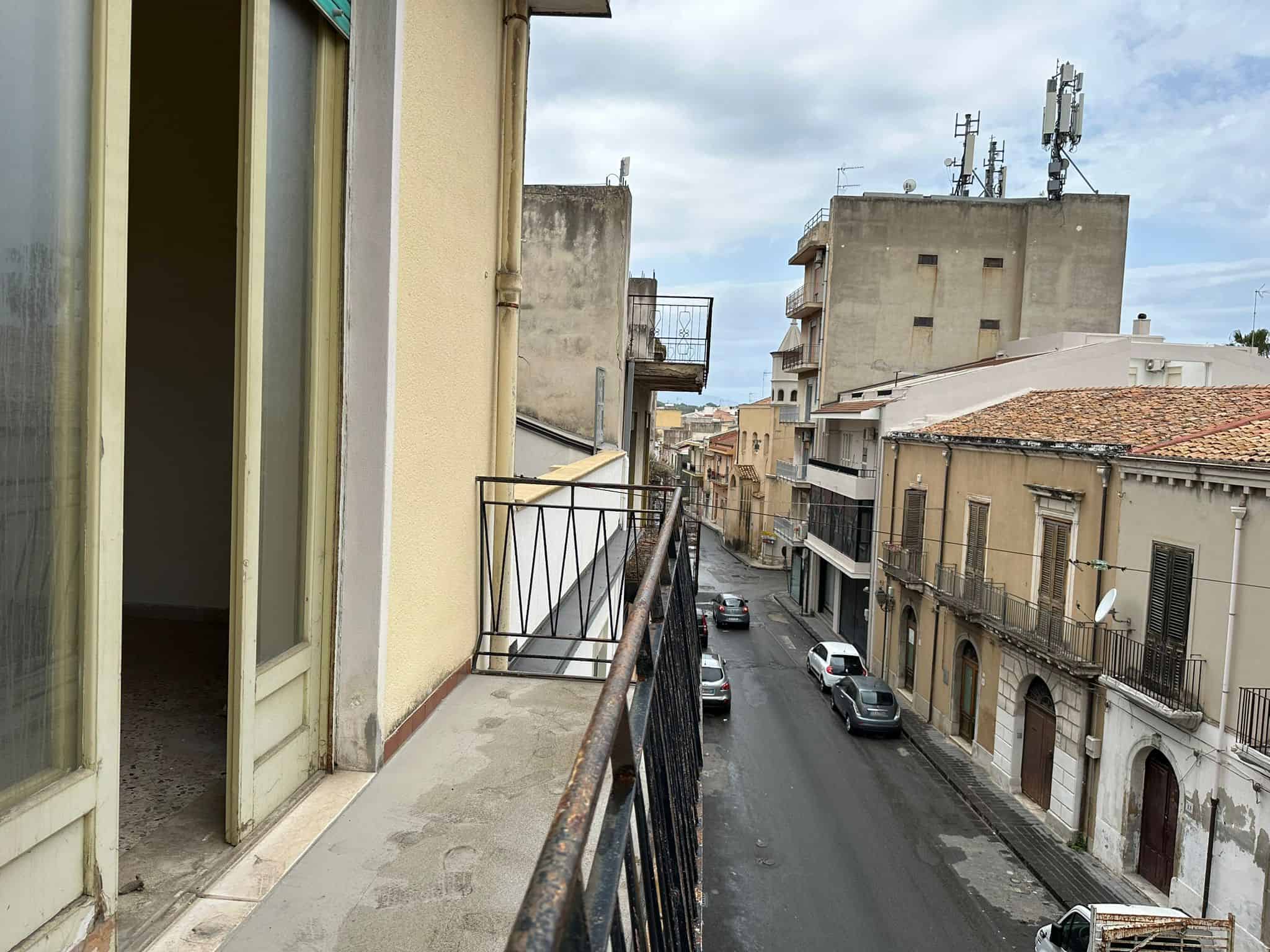 Balcone con vista urbana in via residenziale, in stile classico, con edifici storici, auto parcheggiate e cielo nuvoloso, ideale per immobili e investimenti immobiliari a Napoli.