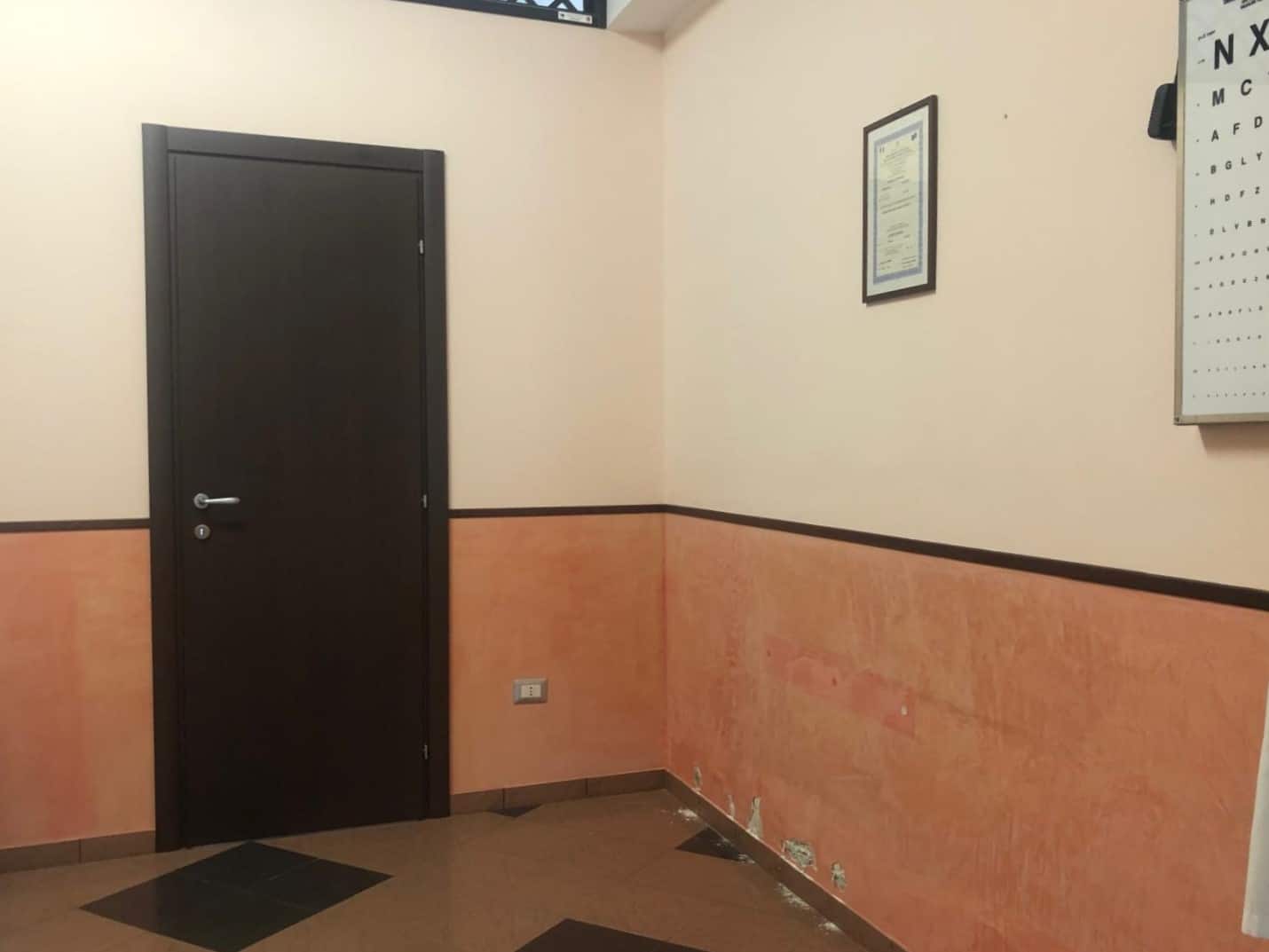 Porta d'ingresso nera e pareti arredate con rivestimento in pannelli di gesso e pannello per attività ottiche. Ideale per ambienti commerciali o studi professionali.