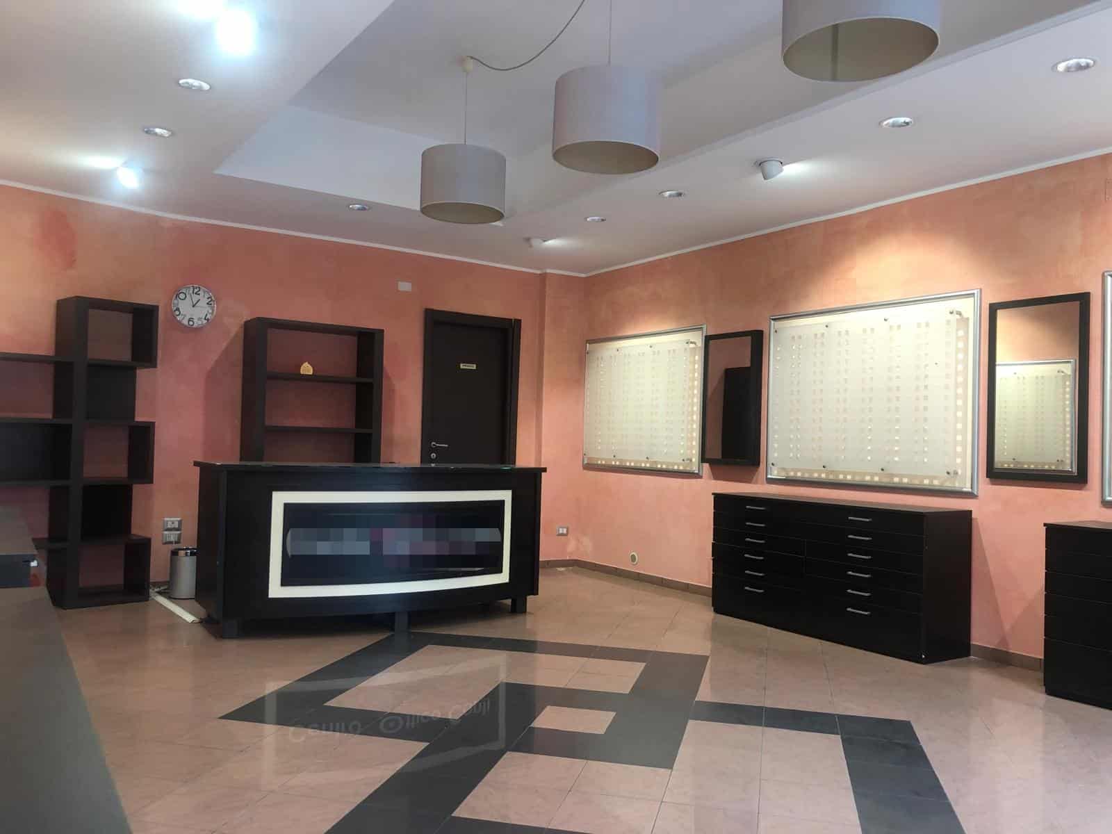 Arredo ufficio moderno con reception e scaffali neri, pareti rosa e grande illuminazione, ideale per spazi professionali e aziende.