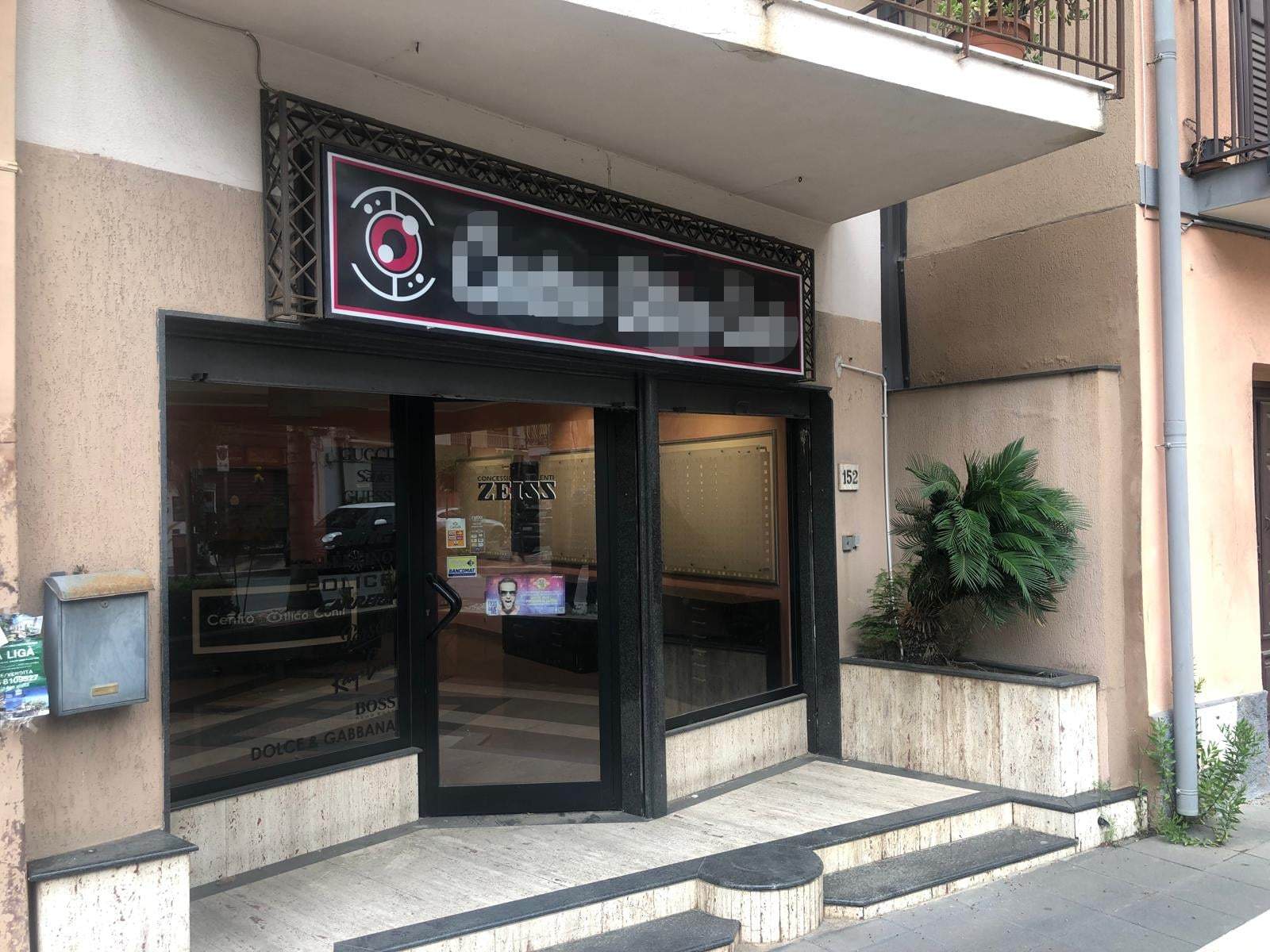 Negozio di servizi di sicurezza e tecnologia con insegna luminosa, vetrina e ingresso su strada, situato in un edificio in zona urbana.