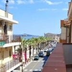 VISTA PANORAMICA DI STRADA RESIDENZIALE A NEXTCASA, VICINO AL MARE, CON PALMI E EDIFICI MODERNI, Cielo AZZURRO E AMBIENTE URBANO TRANQUILLO.