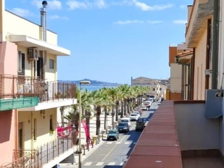 Vasta strada urbana con palme e edifici residenziali, vista mare sullo sfondo, ambiente urbano mediterraneo, architettura moderna, vivace atmosfera cittadina, perfetta per una passeggiata sul lungomare.