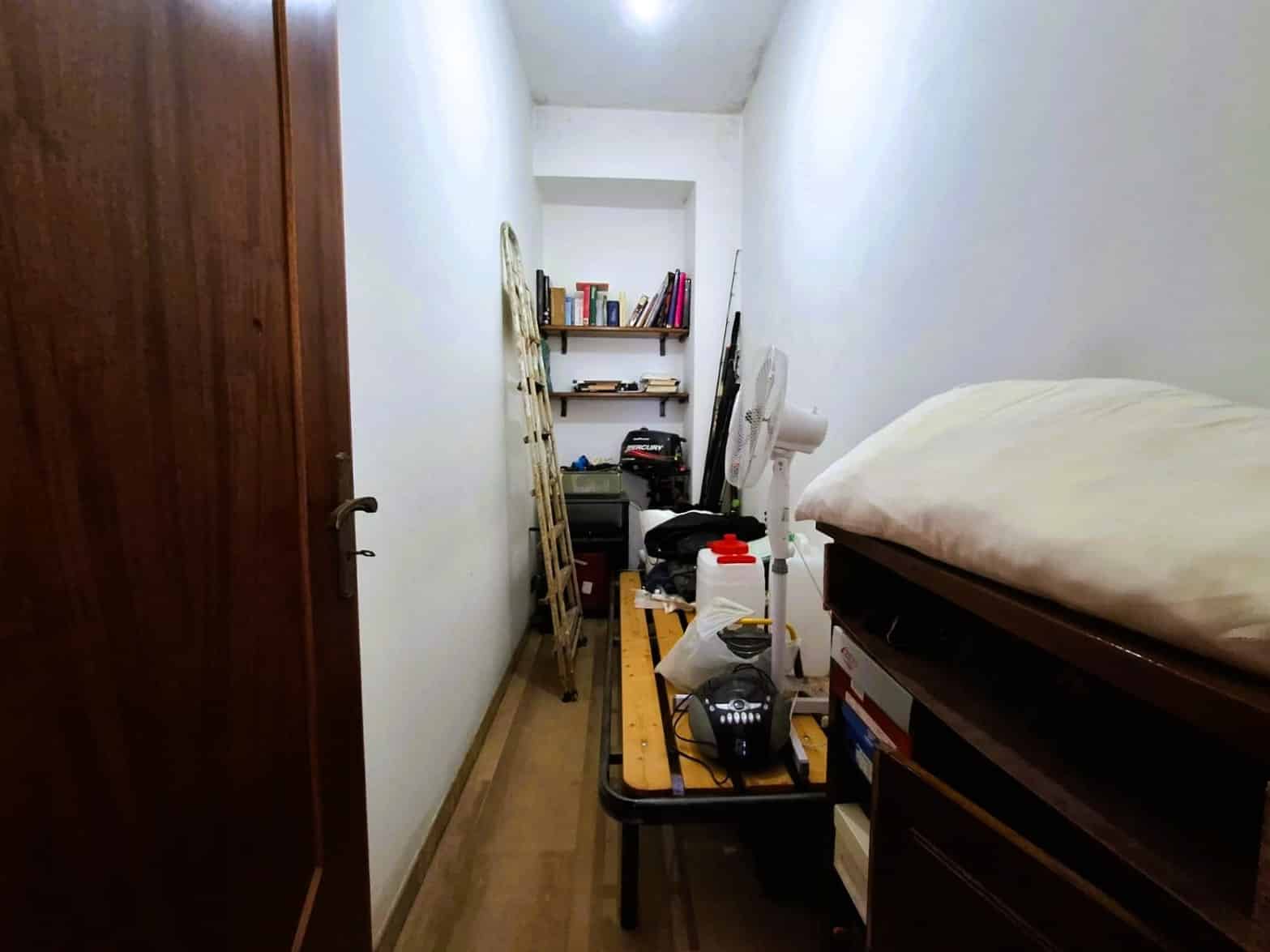 Bundazzo di ripostiglio con scaffale, sedia a scaletta e vari oggetti, in una stanza piccola e funzionale.