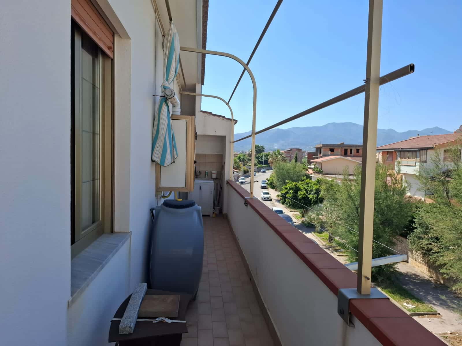 Balcone di un appartamento con vista sulle montagne, arredato con stendibianche, lavatrice e spazio per il bucato, immerso in un contesto residenziale tranquillo e panoramico, ideale per relax e vita quotidiana.