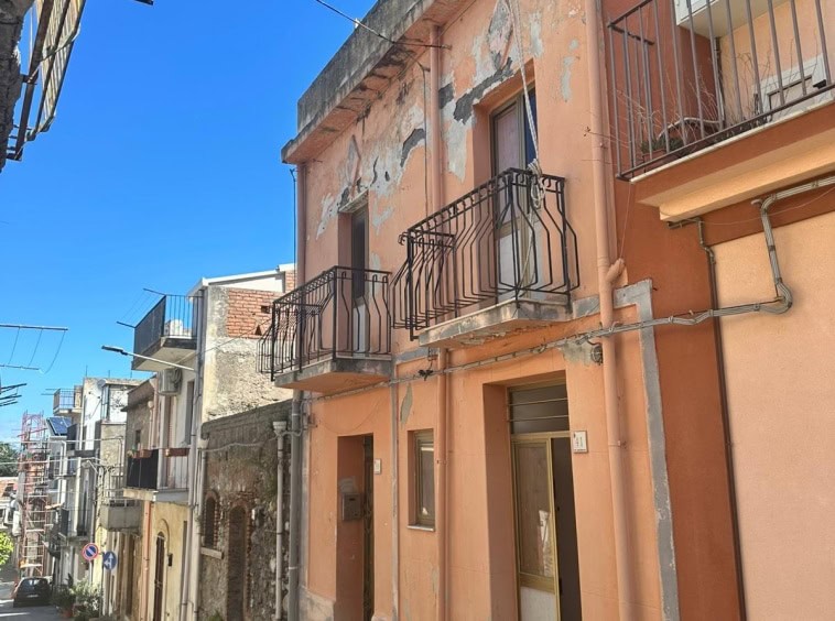 Vecchia casa in stile mediterraneo con facciata in stucco rosa, balconi in ferro battuto e pareti con segni di usura, situata in un vicolo di un quartiere storico.