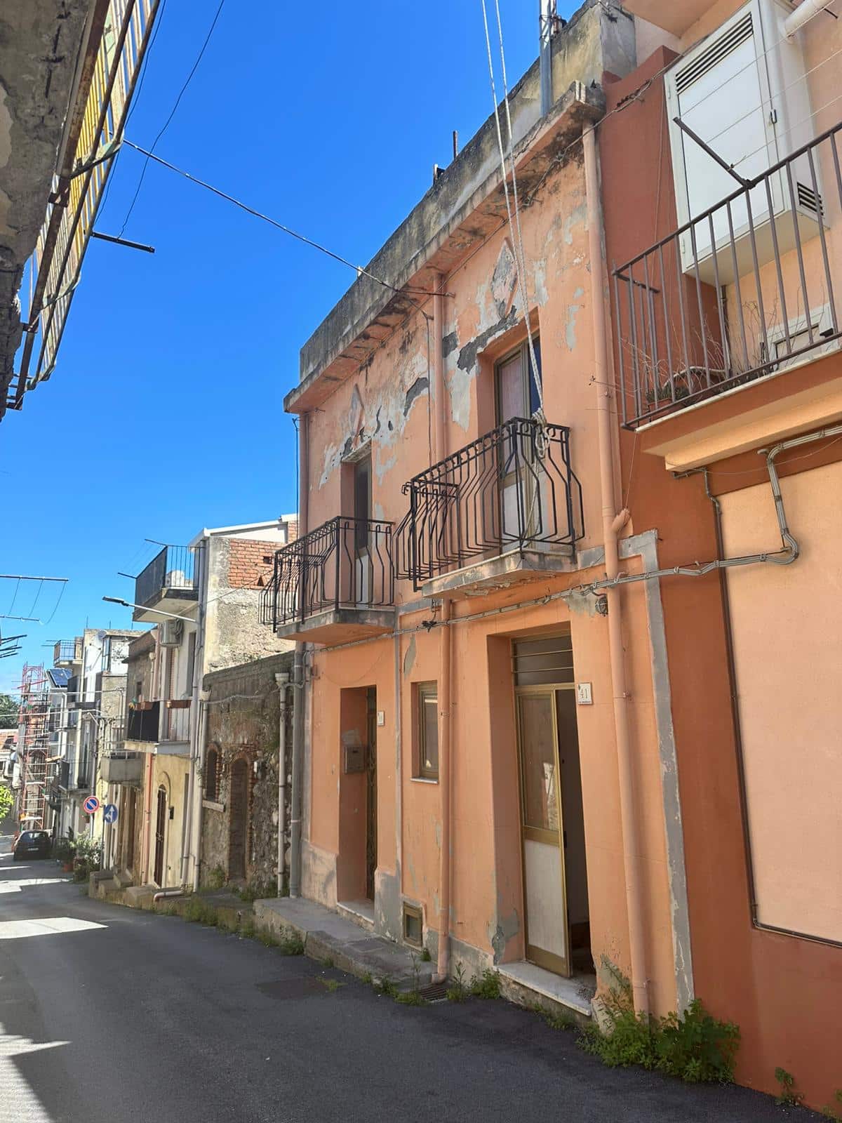 Vecchia casa in stile mediterraneo con facciata in stucco rosa, balconi in ferro battuto e pareti con segni di usura, situata in un vicolo di un quartiere storico.