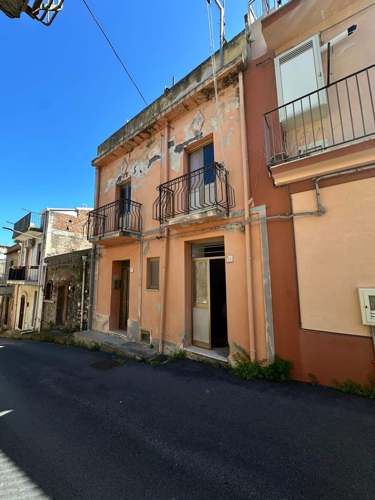 Vecchia casa in stile mediterraneo con facciata colorata e balconi in ferro battuto, zona residenziale soleggiata e da ristrutturare, ideale per investimento immobiliare o progetto di recupero edilizio.