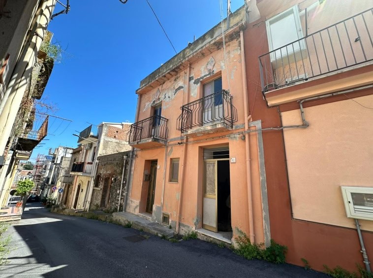 Exteriore di una casa in via urbana con pareti rosa, balconi in metallo e pareti con segni di decadimento, situata in un quartiere storico di Napoli.