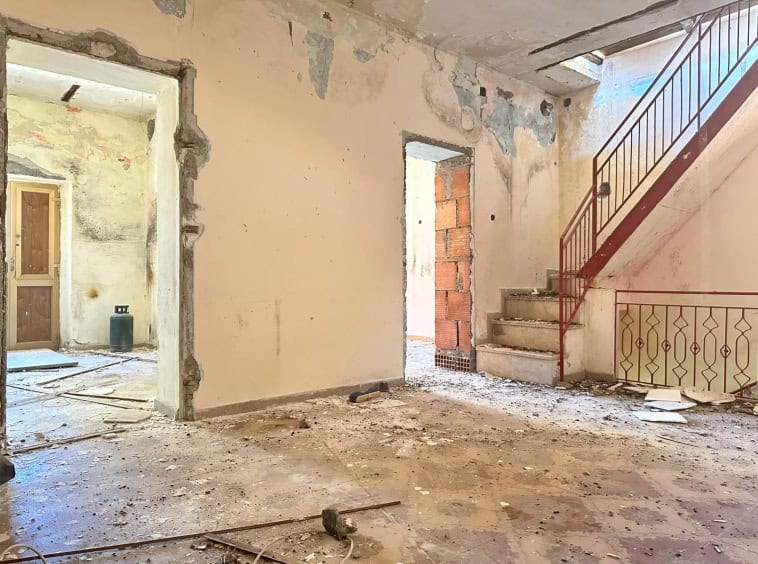 Fugle di sottofondo di un appartamento in ristrutturazione, con muri sbozzati e pavimento in cemento, scala in ferro e pareti con tracce di vernice, pronto per il restauro.