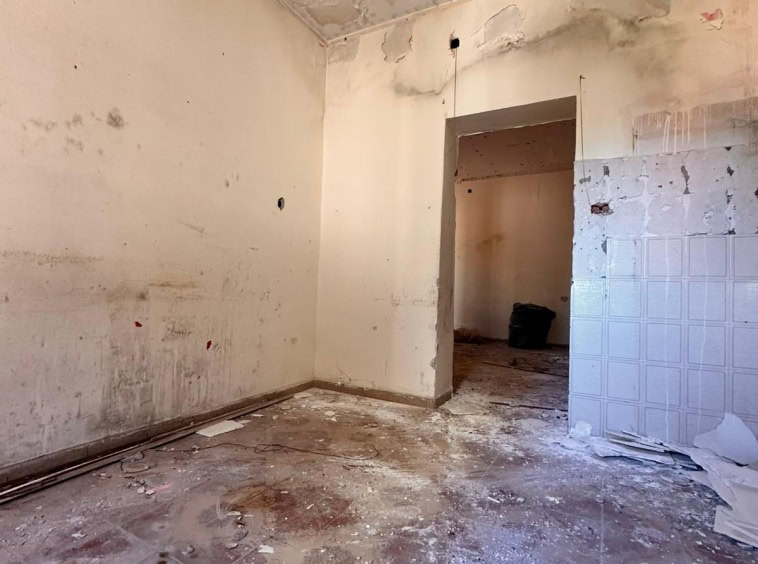 Pareti e soffitto in fase di ristrutturazione di un appartamento, con evidenti segni di umidità e danni, pavimento sporco e lavori in corso per una futura riqualificazione edilizia.