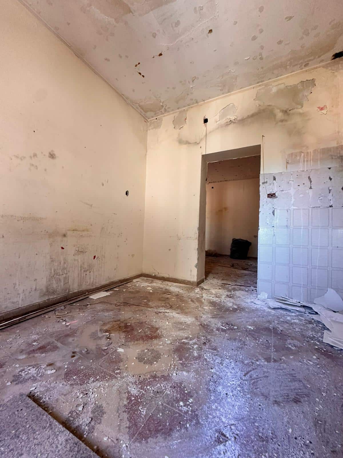 Pareti e soffitto in fase di ristrutturazione di un appartamento, con evidenti segni di umidità e danni, pavimento sporco e lavori in corso per una futura riqualificazione edilizia.
