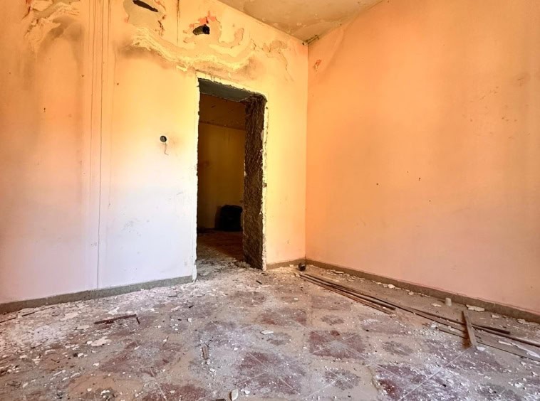 Un'immagine di una stanza in ristrutturazione con pareti rosa e pavimento con detriti e polvere, pronta per lavori di rinnovamento e arredamento, rappresentando opportunità di ristrutturazione immobiliare.