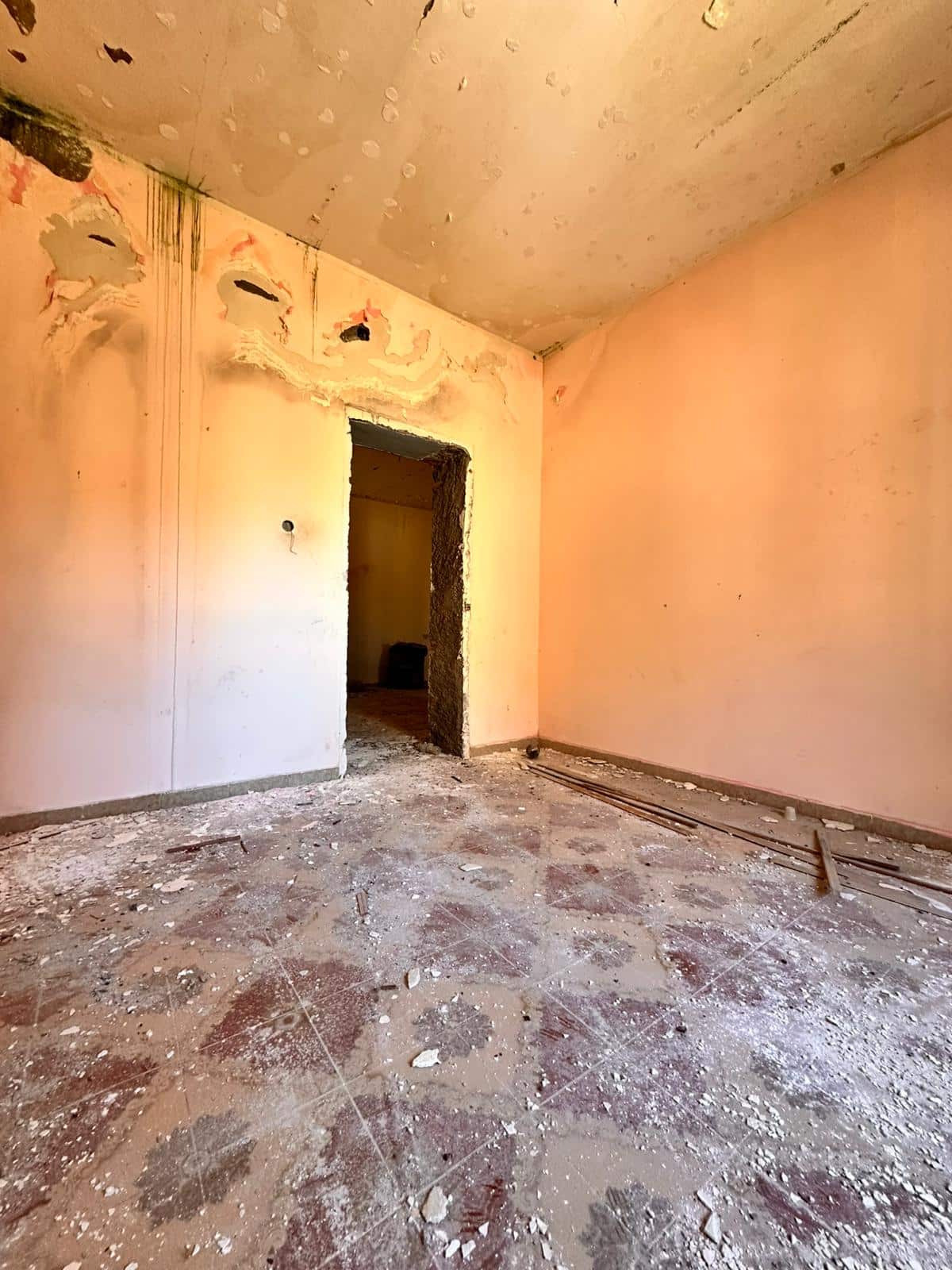 Un'immagine di una stanza in ristrutturazione con pareti rosa e pavimento con detriti e polvere, pronta per lavori di rinnovamento e arredamento, rappresentando opportunità di ristrutturazione immobiliare.