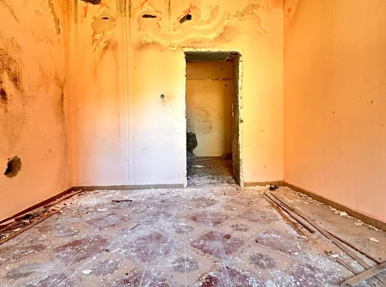 Vecchio interno di casa in fase di ristrutturazione, muri con segni di maltempo, pavimento in rovina, lavori di rifacimento in corso.