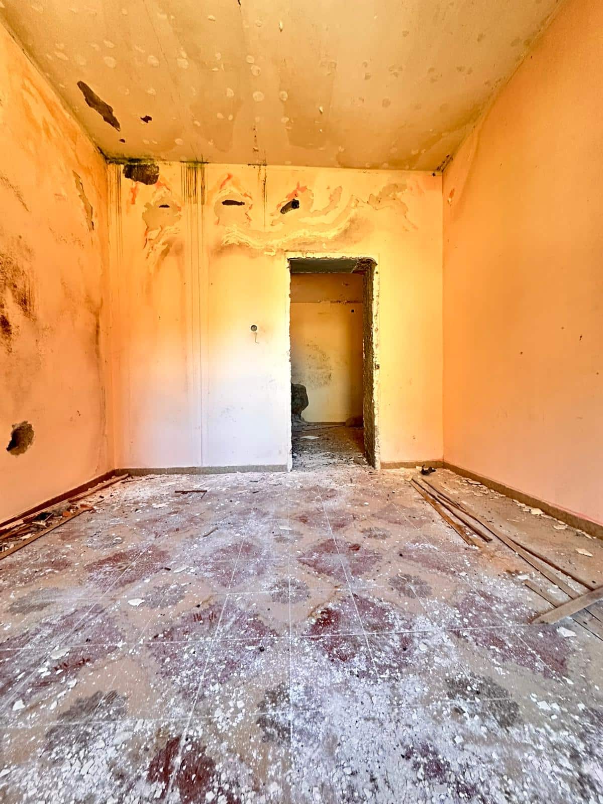 Vecchio interno di casa in fase di ristrutturazione, muri con segni di maltempo, pavimento in rovina, lavori di rifacimento in corso.