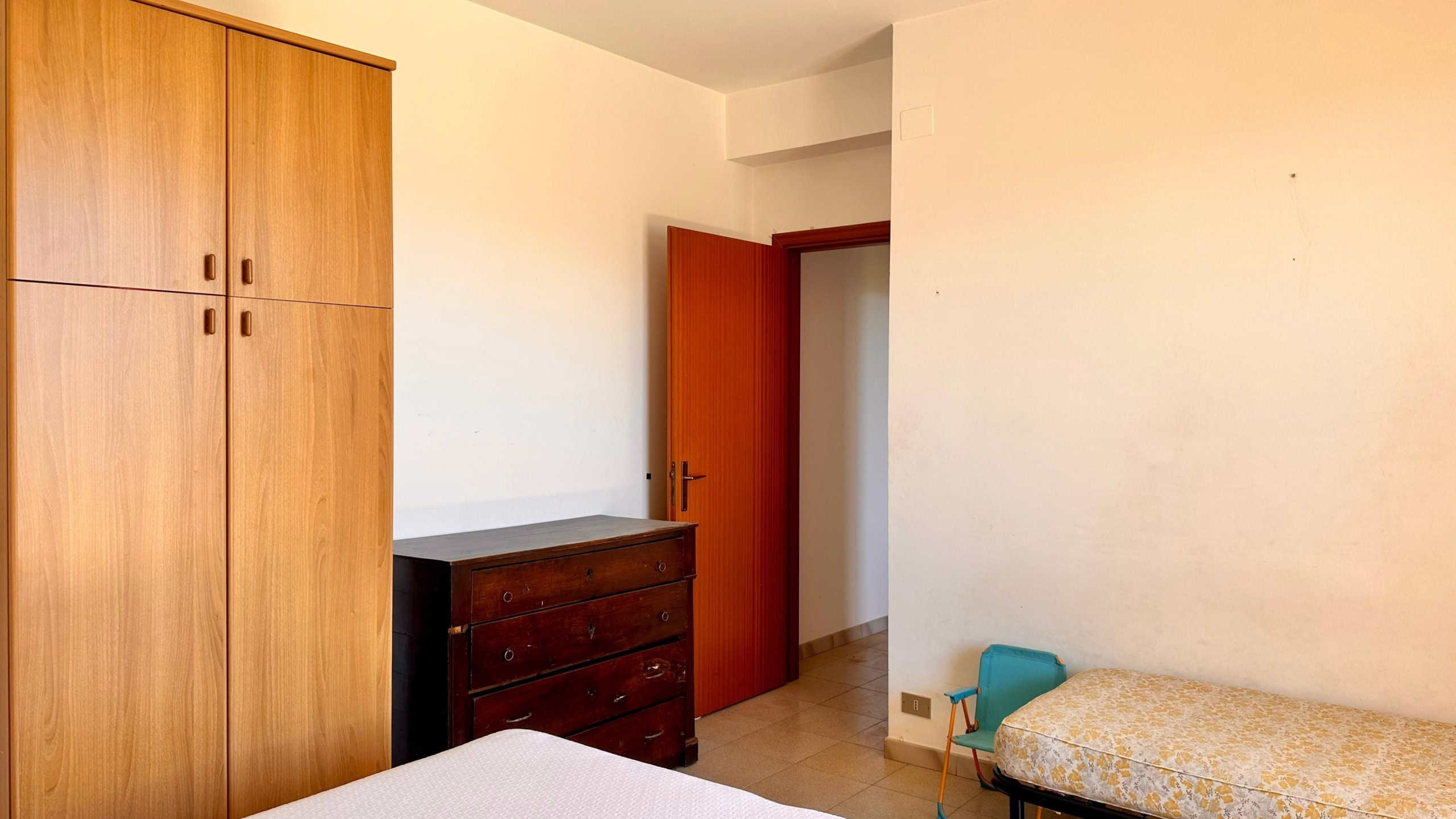 Armadio a due ante in legno, camera da letto semplice con cassettiera antica e letto singolo con copriletto giallo e bianco.