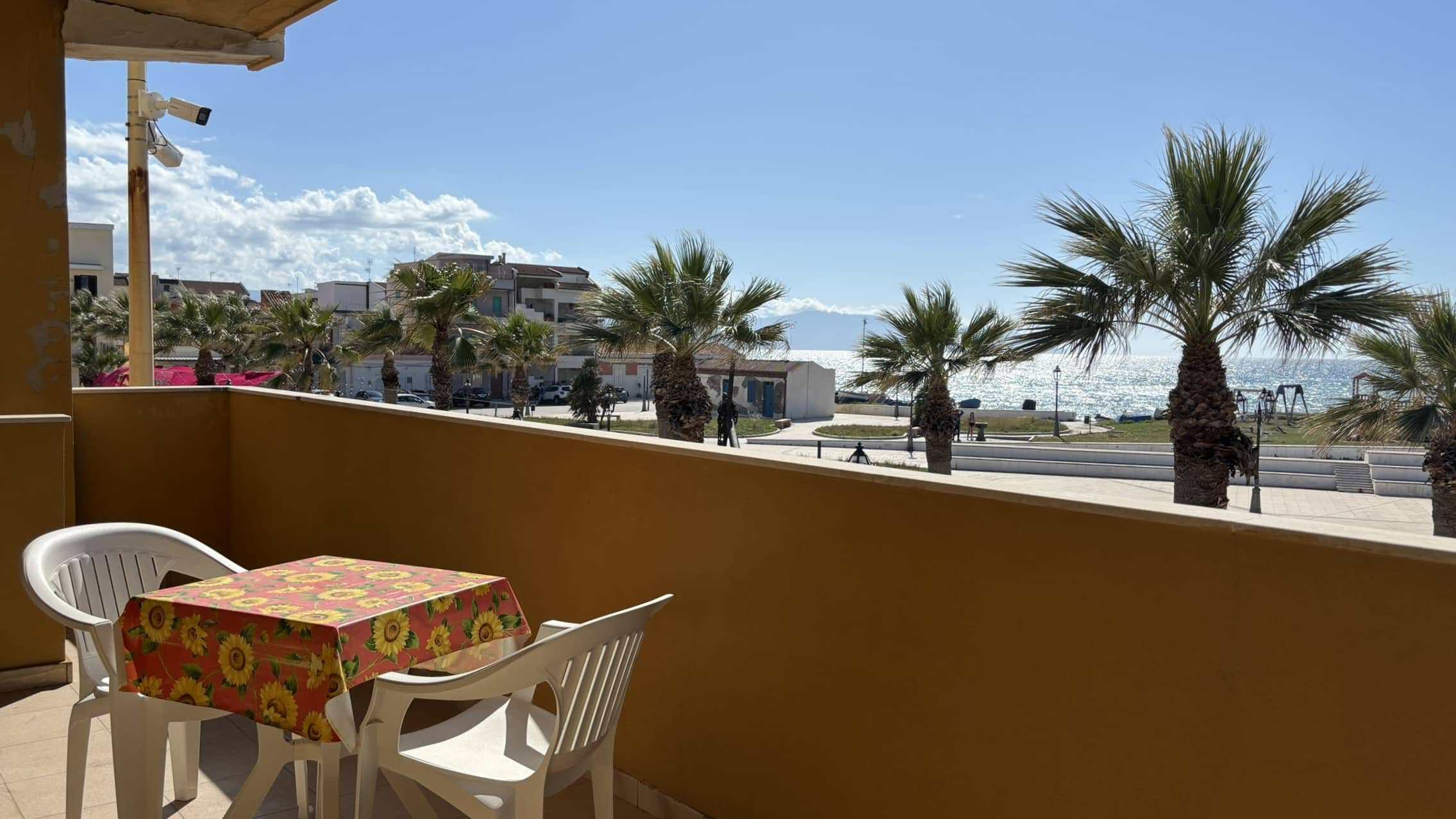 Vista mare dal balcone di un appartamento vicino alla spiaggia con palme e area relax all'aperto in stile mediterraneo a NextCasa.