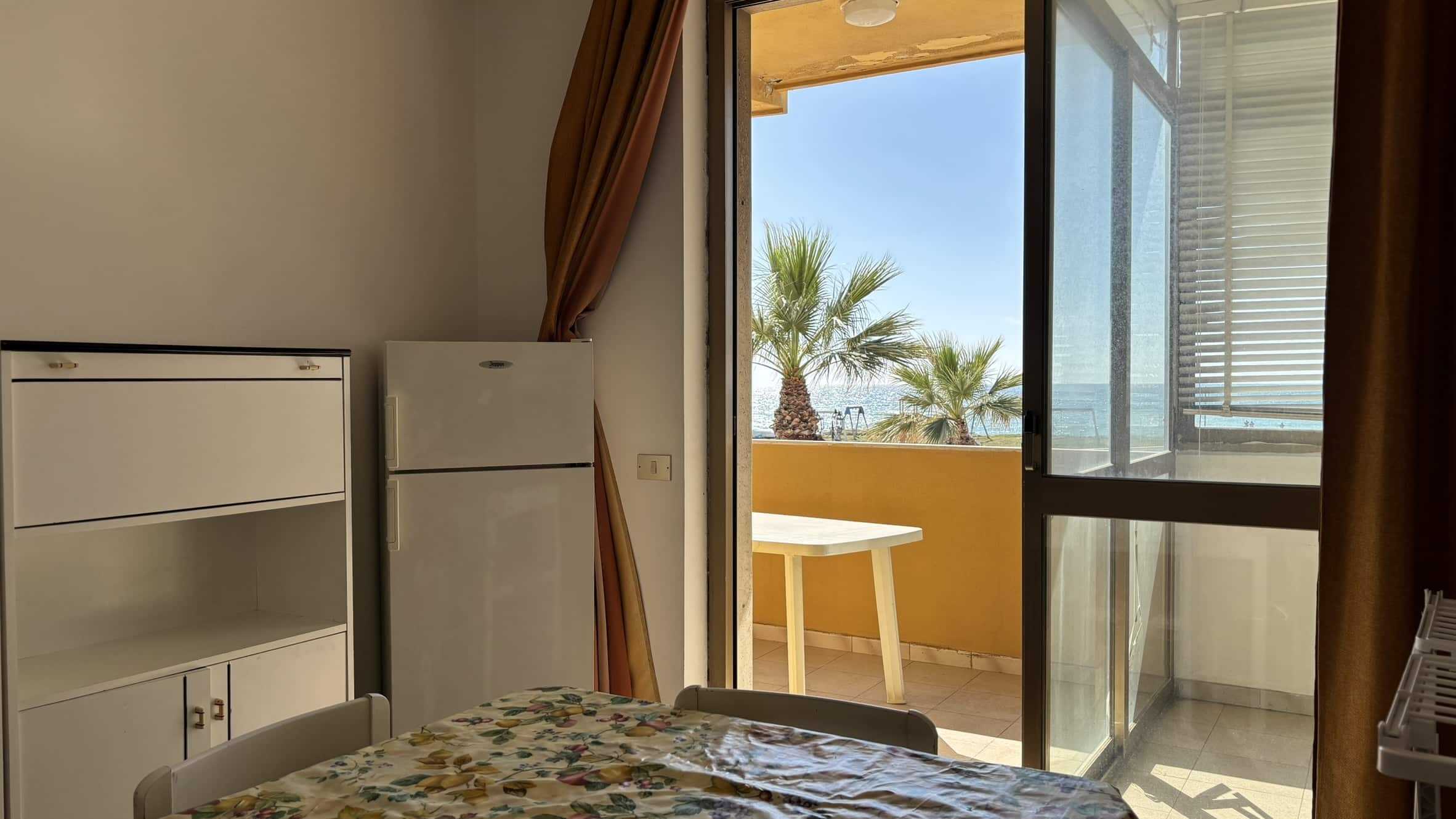 Vista della camera con balcone vista mare, arredamento semplice e spazi luminosi, ideale per vacanze al mare.