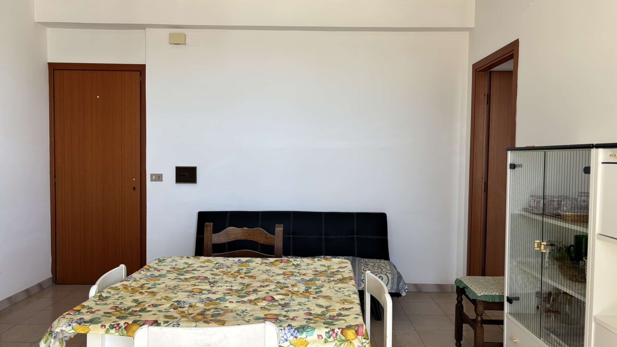 Tavolo da pranzo con tovaglia floreale in soggiorno, mobili pratici e decorazioni essenziali in casa NextCasa, ambiente accogliente e funzionale per vivere al meglio i tuoi momenti quotidiani.