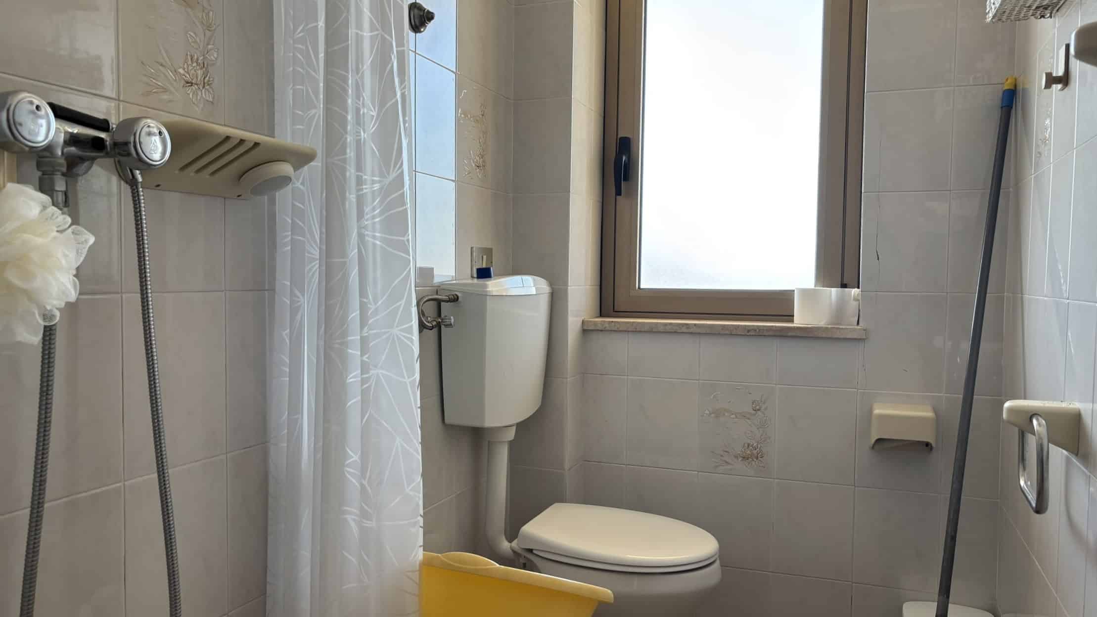 Lavabo e servizi igienici in bagno con finestra, accessori per disabili, piastrelle color beige, lavanderia e dettagli funzionali toeletta, ideale per residence NextCasa.