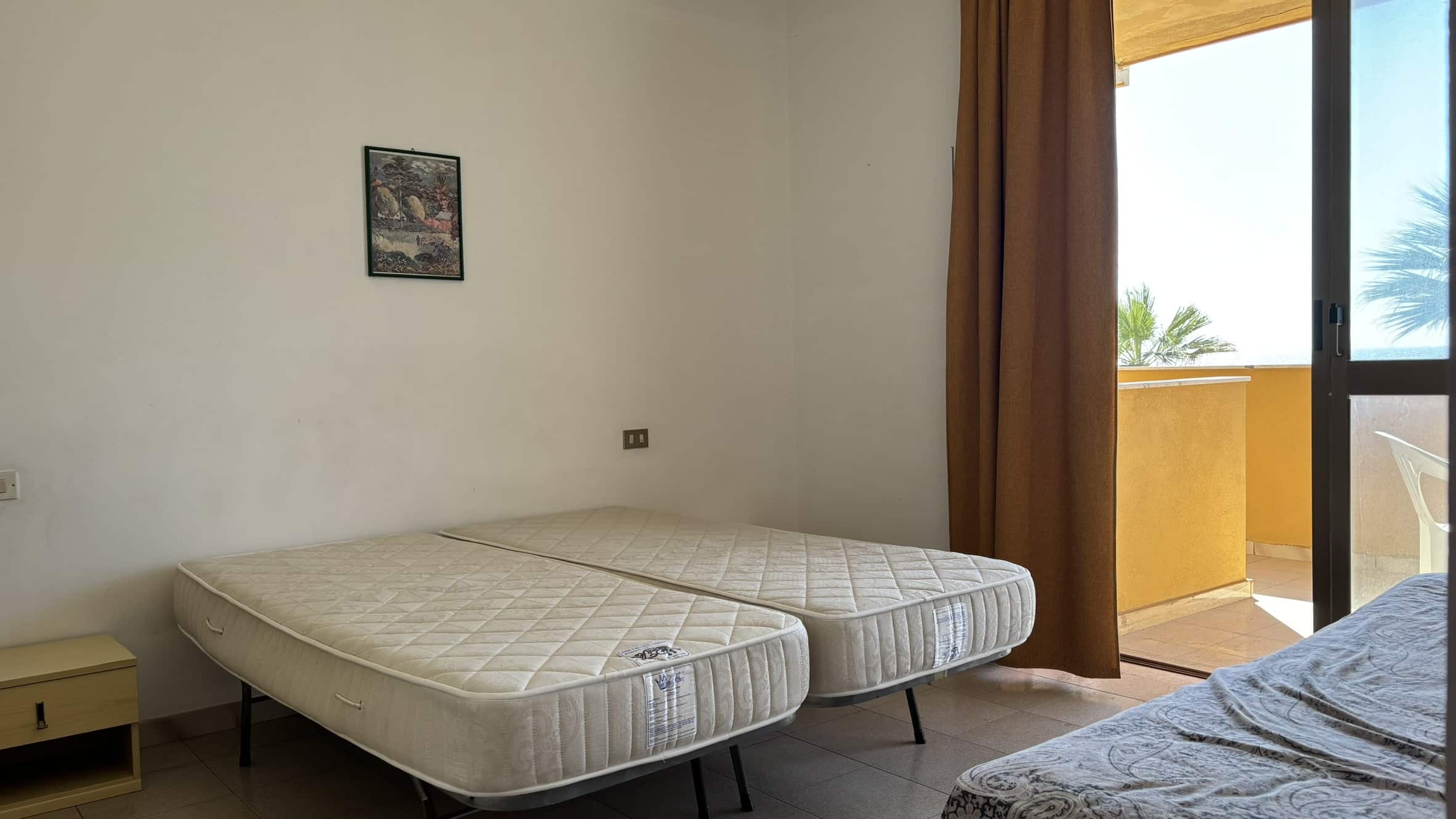 Letto matrimoniale con rete a doghe e camera da letto arredata moderna in appartamento vicino al mare. Vista sul balcone con accesso alla terrazza soleggiata, ideale per vacanze al mare.