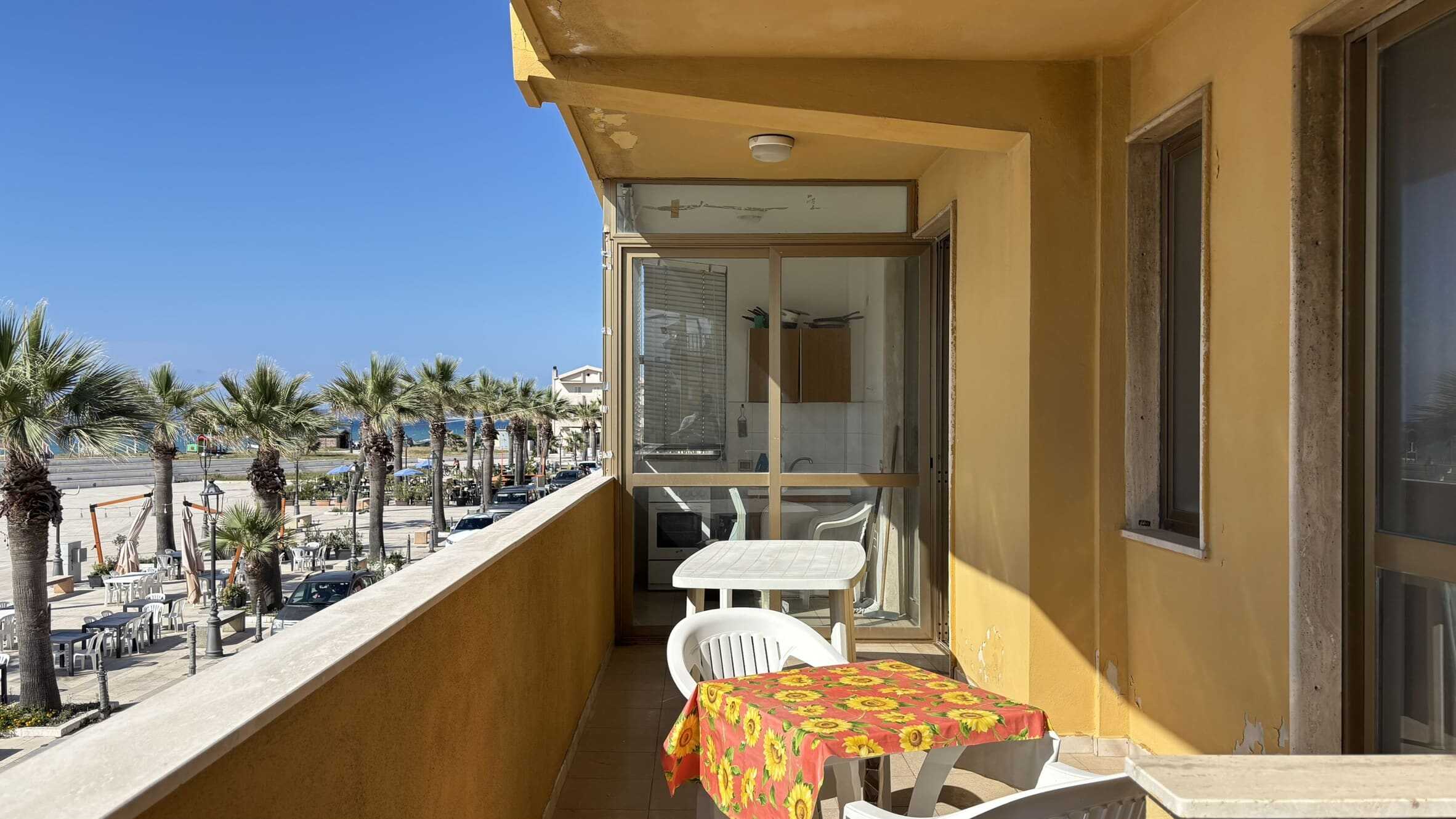 Balcone di un appartamento con vista mare e area esterna arreddata per relax in estate, con fiori di girasole sul tavolo.