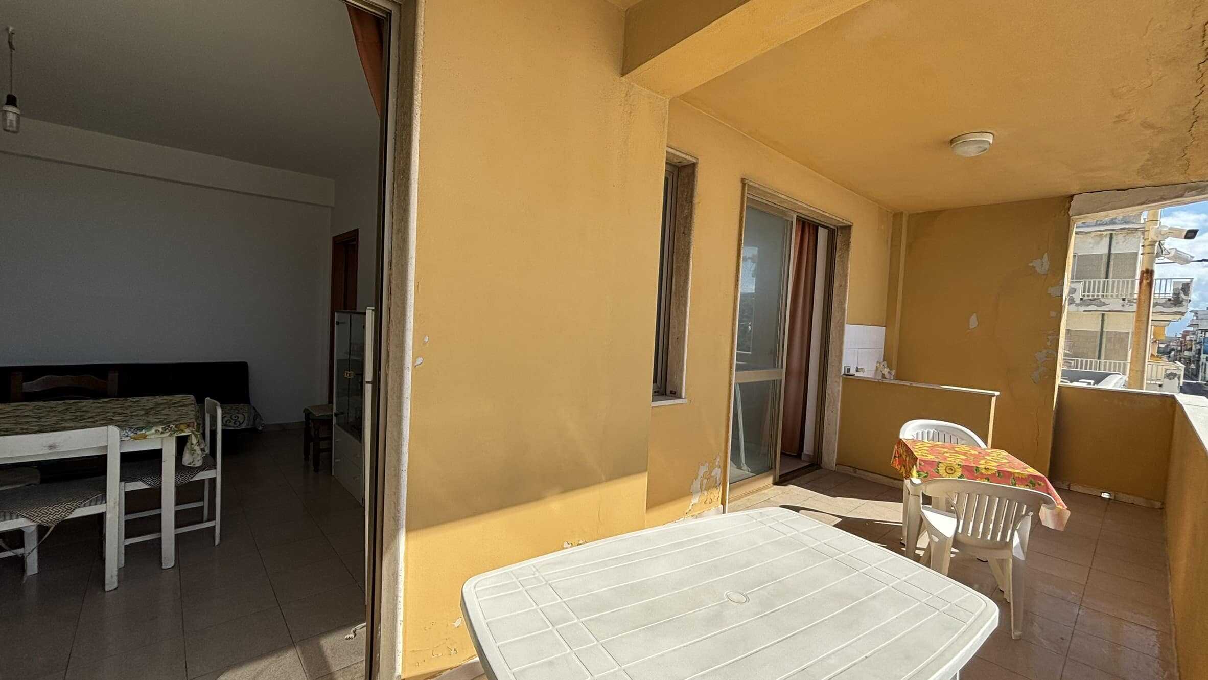 Balcone di un appartamento in zona urbana con mobili di plastica, viste sulla città e muri con segni di usura, luce naturale, atmosfera informale e residenziale.