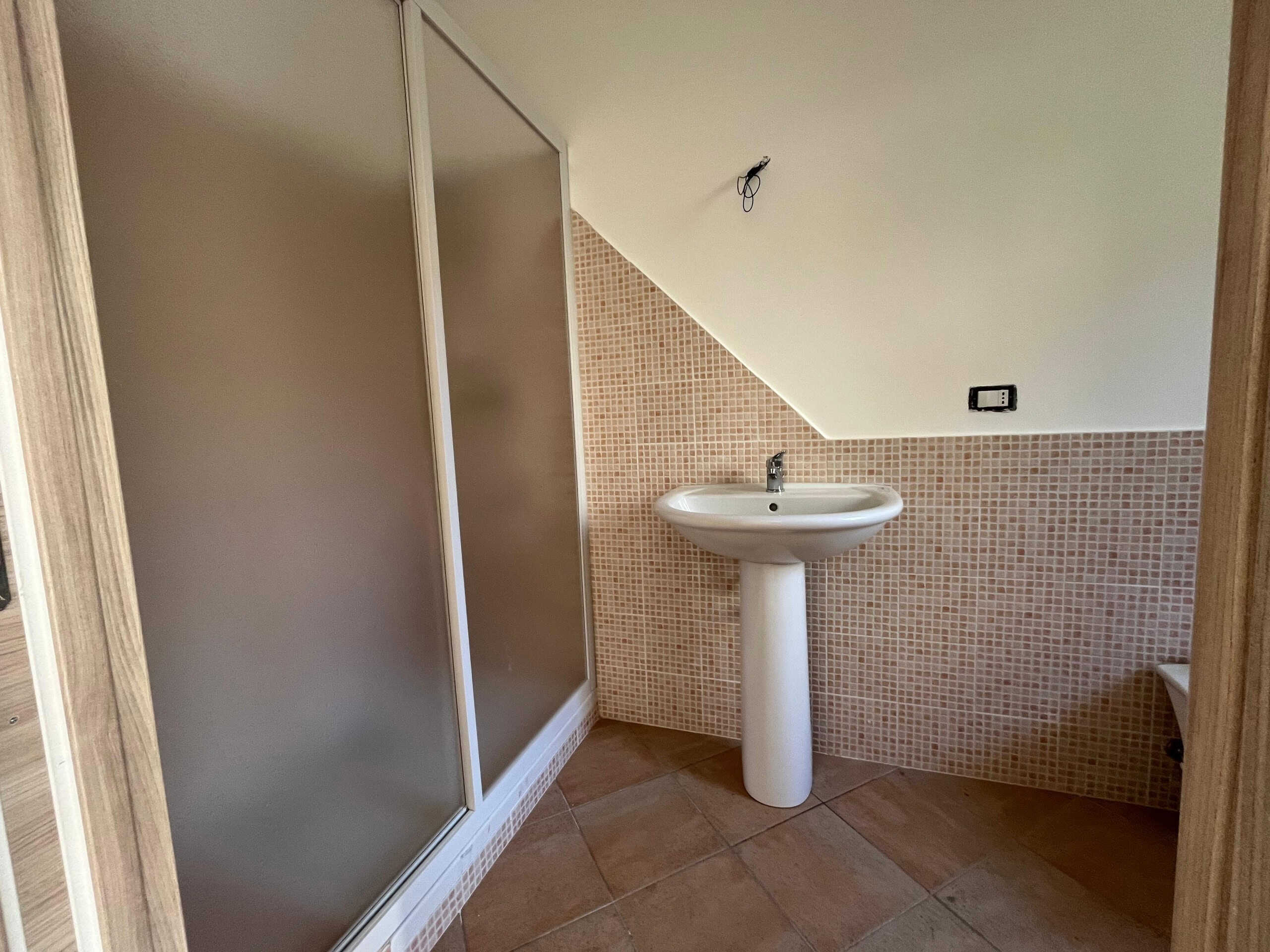 Lavabo e doccia in bagno moderno con piastrelle beige e arredo semplice, ideale per casa in vendita o affitto.