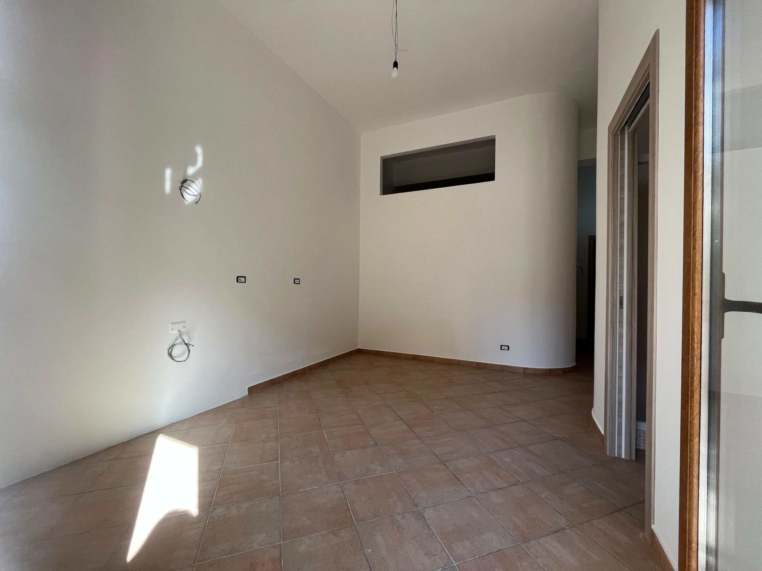 Interno di un appartamento in costruzione o ristrutturazione, con pareti bianche, pavimento in piastrelle e impianto elettrico visibile, pronto per essere arredato.
