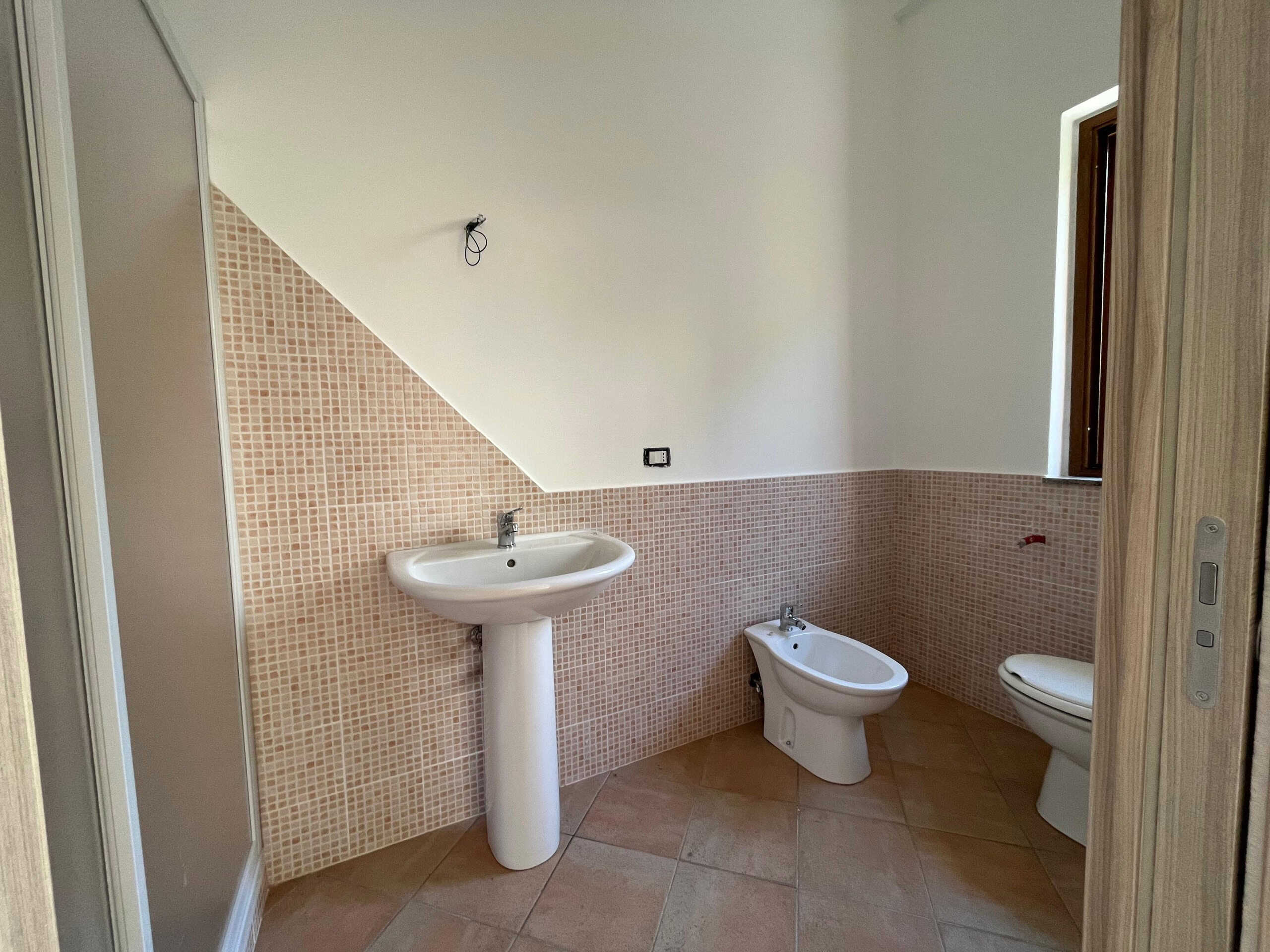 Lavabo e WC in bagno ristrutturato con piastrelle rosa e parete bianca, bagno di design con finiture moderne e luce naturale, ideale per abitazioni di nuova costruzione o ristrutturazione.