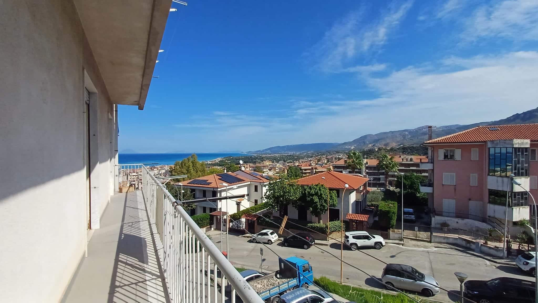Balcone di un appartamento con vista mare e sui tetti delle case della costa, in una giornata soleggiata e serena, con un paesaggio panoramico tra cielo e mare.