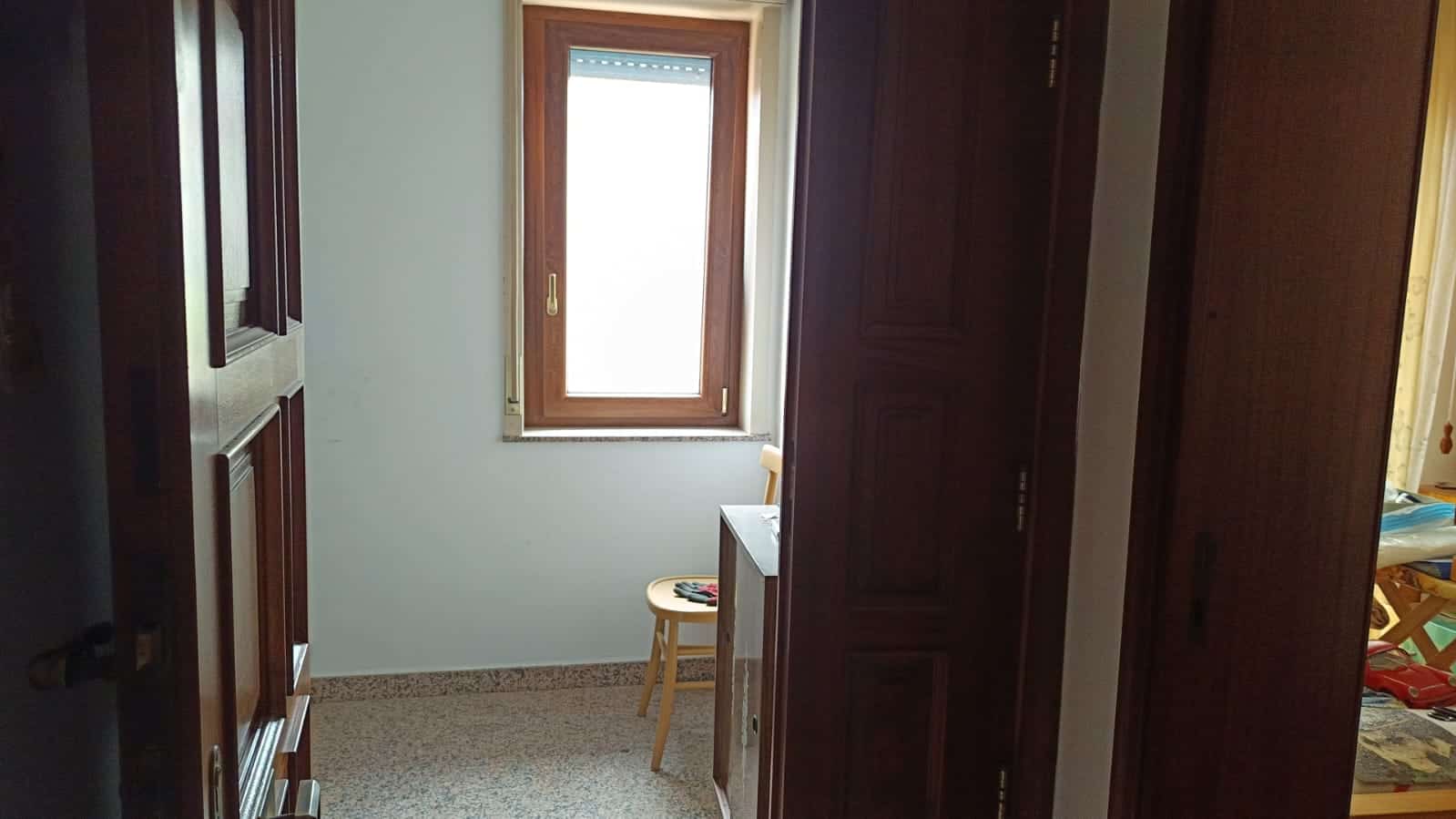 Aspetto di un angolo di una stanza con armadi in legno scuro e finestra con cornice in legno naturale, ambiente interno domestico.