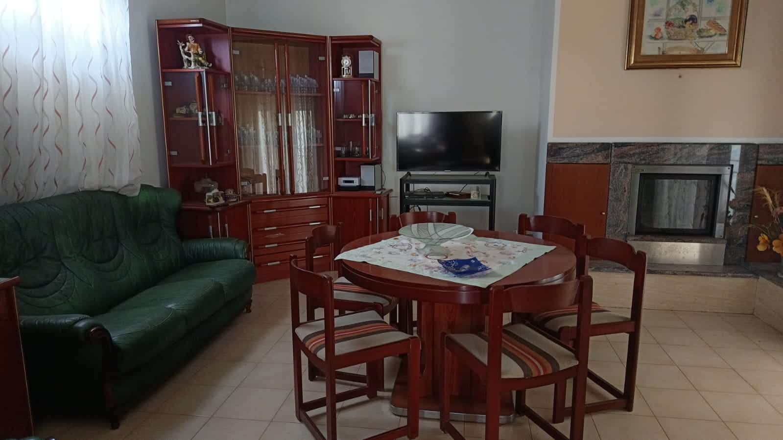 Risorsa per interni di soggiorno con parete divano in pelle verde, tavolo rotondo con sedie, grande mobile in legno, televisore e camino in pietra, arredamento classico e accogliente.