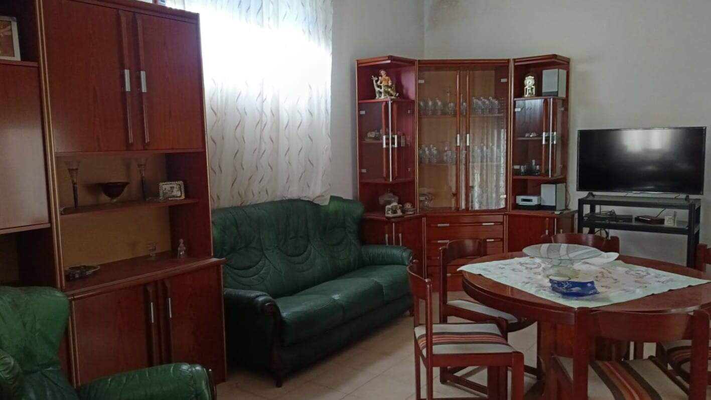 Mobili soggiorno in legno, divani in pelle verde, tavolo da pranzo rotondo con sedie, arredamento classico, casa con soggiorno elegante, display in vetro con cristalli, TV schermo piatto, esposizione di oggetti decorativi, interni confortevoli, NextCasa.
