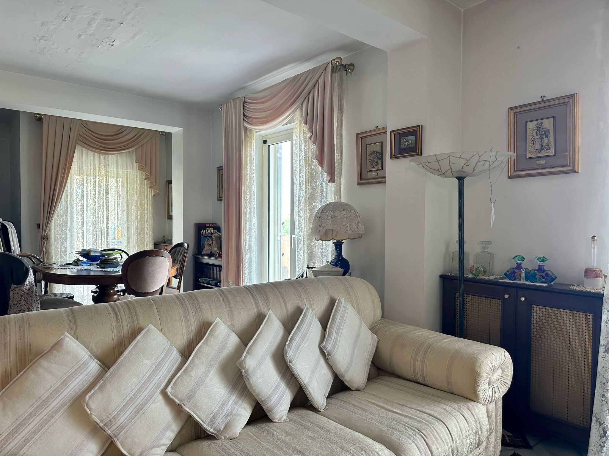 Divano classico beige con cuscini coordinati in soggiorno, con tende e cornici d'epoca, ambiente accogliente e elegante, dettagli di arredamento vintage, stile tradizionale e comfort abitativo.