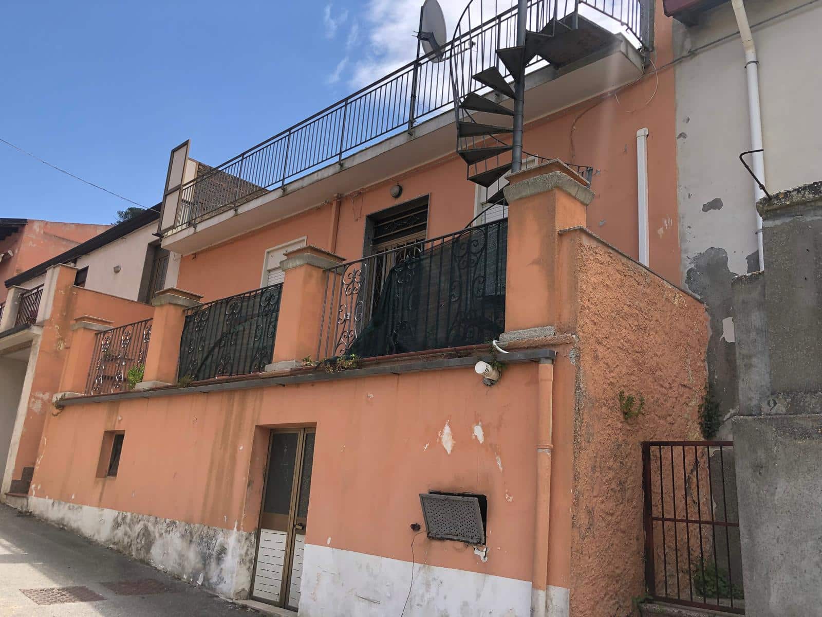 Insediamento residenziale con balconi e scale esterne in stile classico, costruzione in muratura con veranda e grate di sicurezza, situato in zona urbana di prossimità ai servizi, ed è adatto sia come prima casa che come investimento immobiliare.