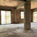 Ampio spazio interno di un appartamento in costruzione con pareti in mattoni rossi, colonne in cemento e grandi finestre con balcone, pronto per rifiniture.