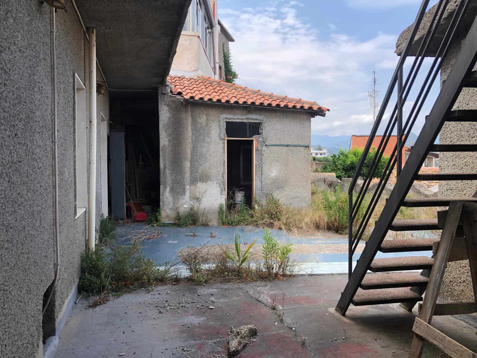 Vecchio spazio esterno di una proprietà in demolizione o ristrutturazione, con erba e piante cresciute, e scale in legno. Potenziale rinnovamento immobiliare, investimento per property upgrade.