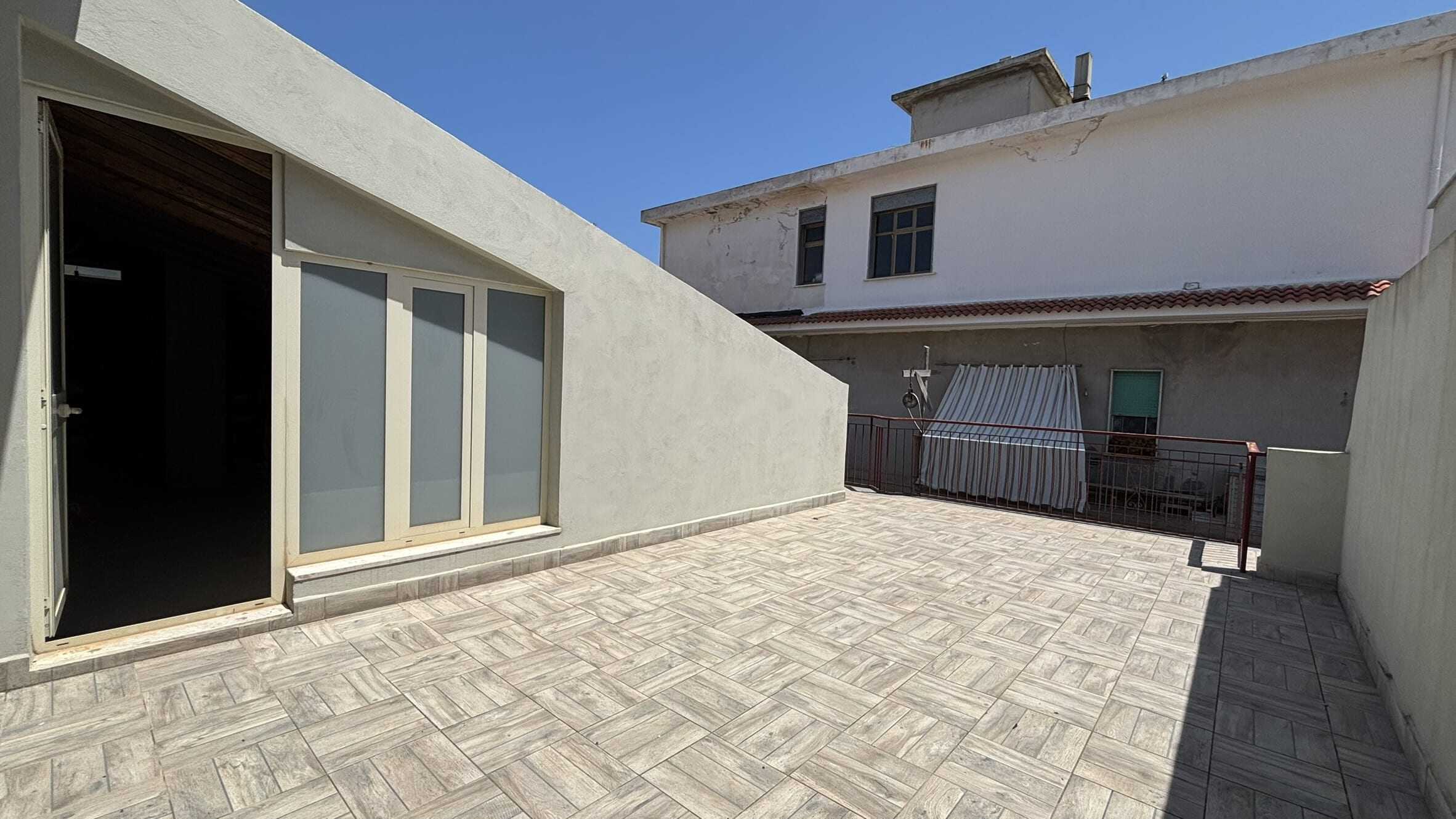 Ampio terrazzo con pavimentazione in piastrelle, spazio esterno ideale per relax e convivialità, con vista sulle facciate di edifici limitrofi e ambiente soleggiato, situato in zona residenziale.