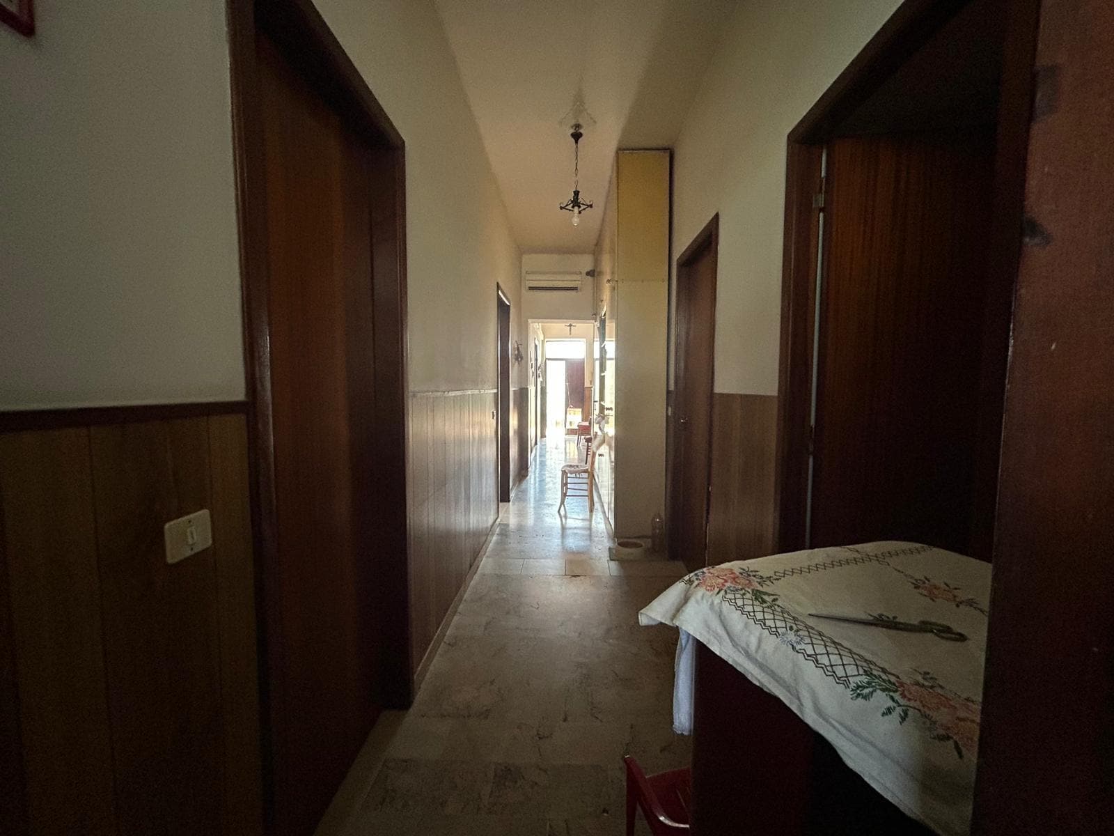 Spazi interni di una casa con pareti in legno e un corridoio che porta a una zona giorno luminosa, con mobili essenziali e atmosfera accogliente, ideale per ambienti familiari e residenziali.